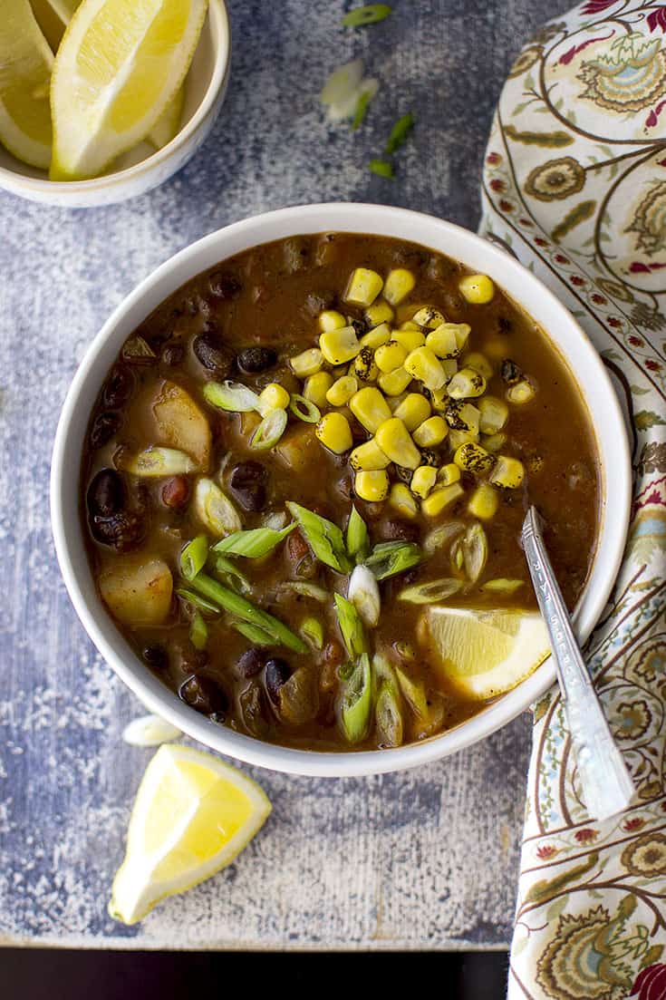 Bowl of Black bean veggie soup with roasted corn and lemon wedges
