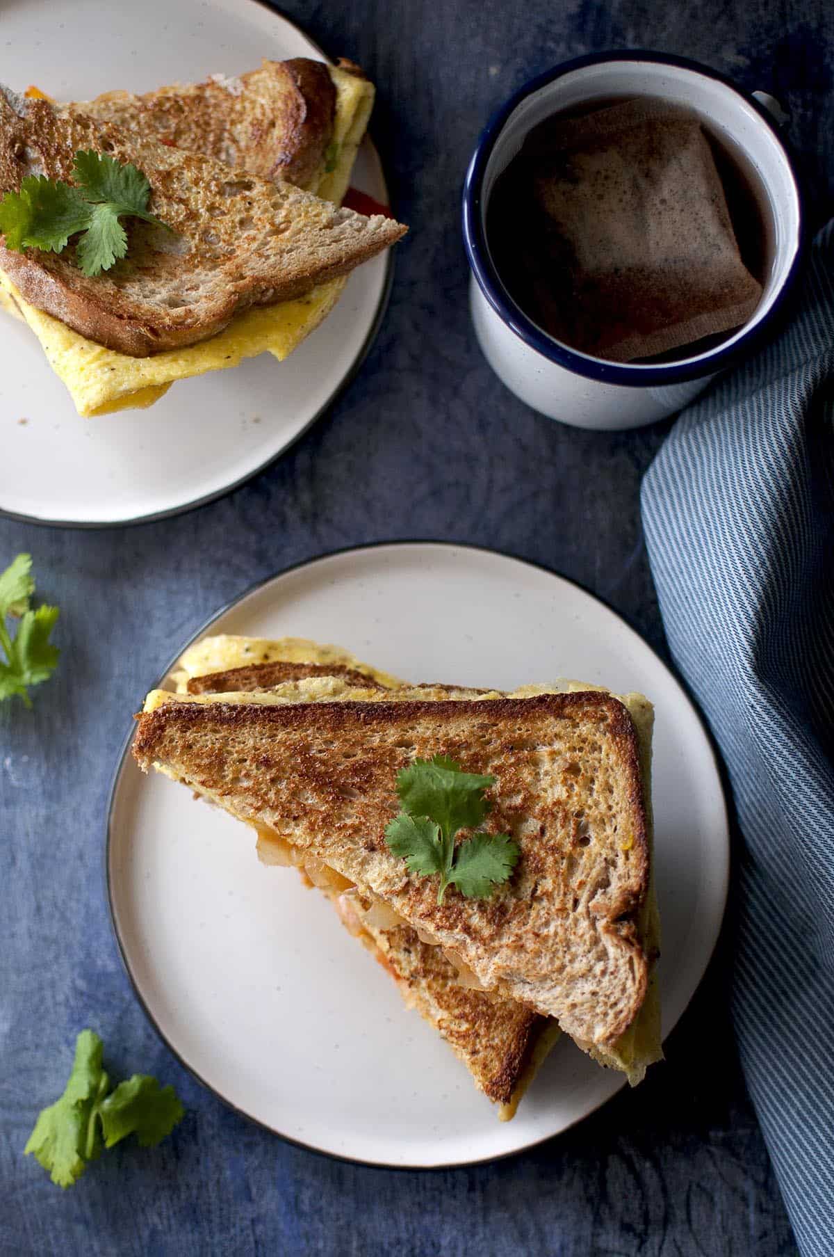 Top view of egg toast sandwich on a white plate with a enamel mug with tea in the background