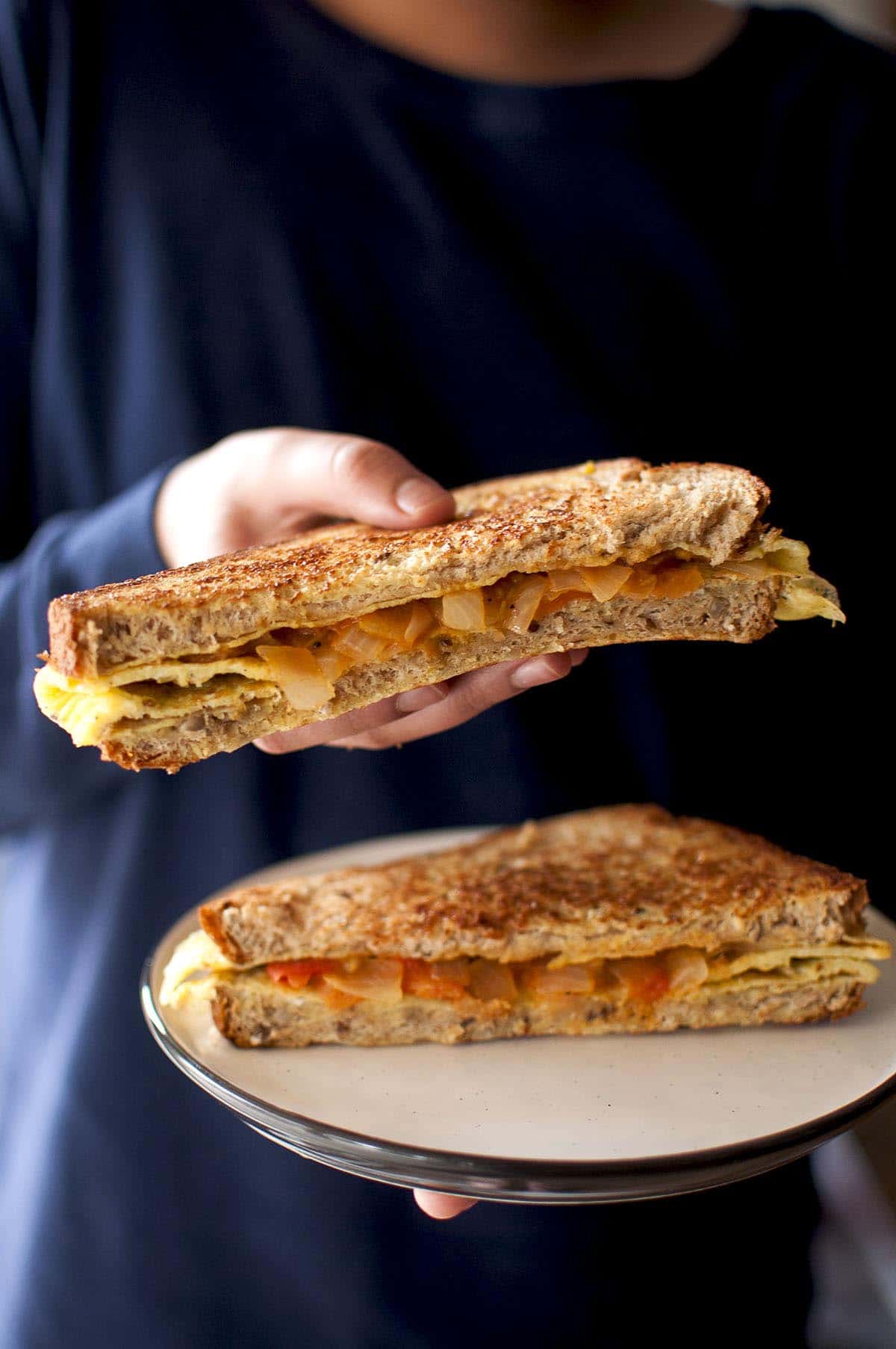 Kid holding half a bread omelet sandwich in one hand and plate with the other half in another hand