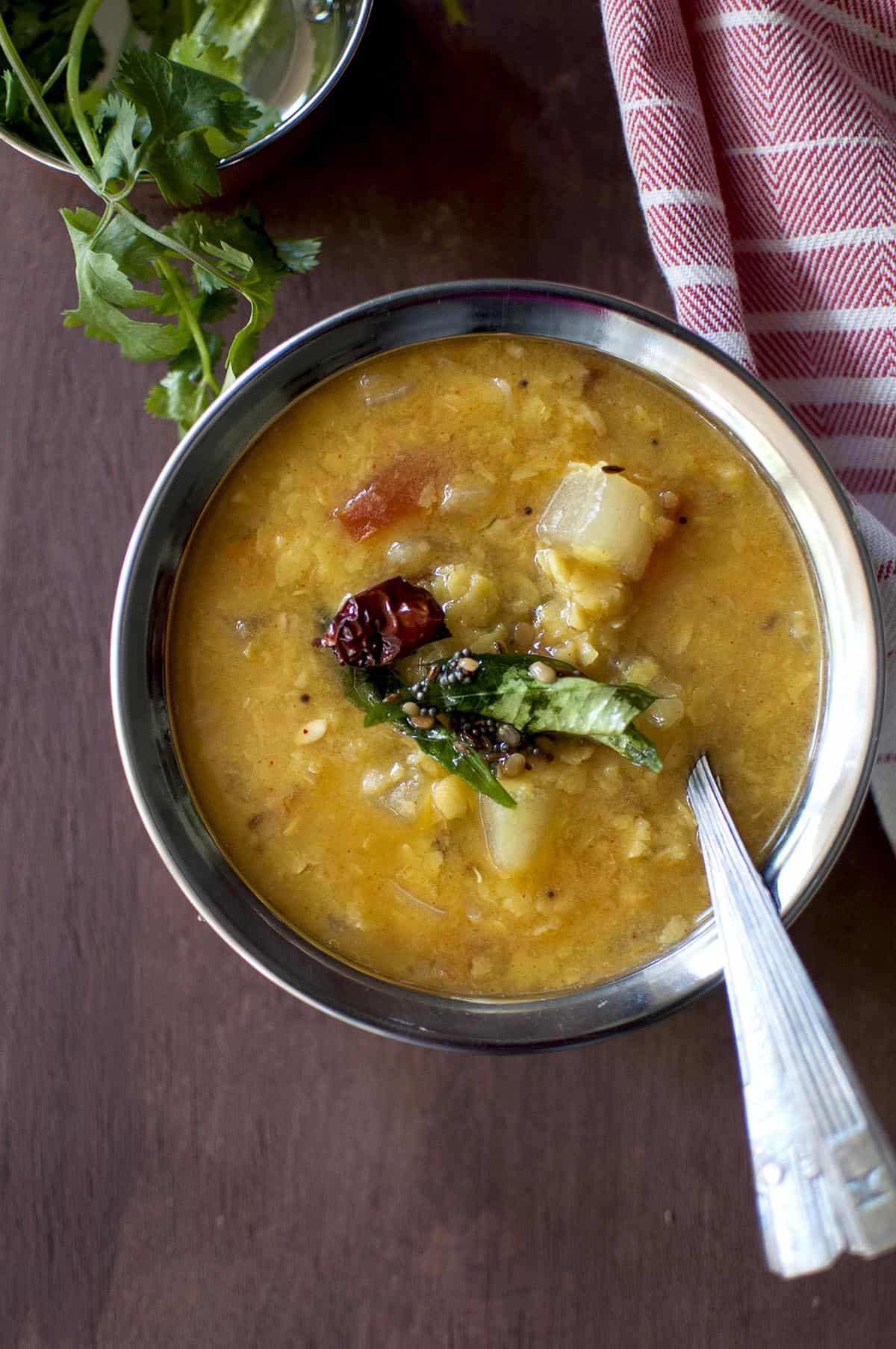 steel bowl with dosakaya pappu topped with tempering and a spoon inside