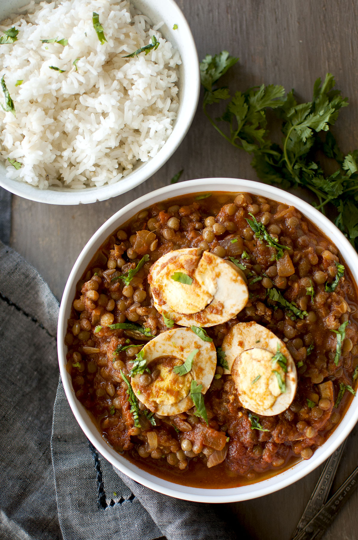 White bowl with lentils curry topped with egg halves served with a bowl of white rice