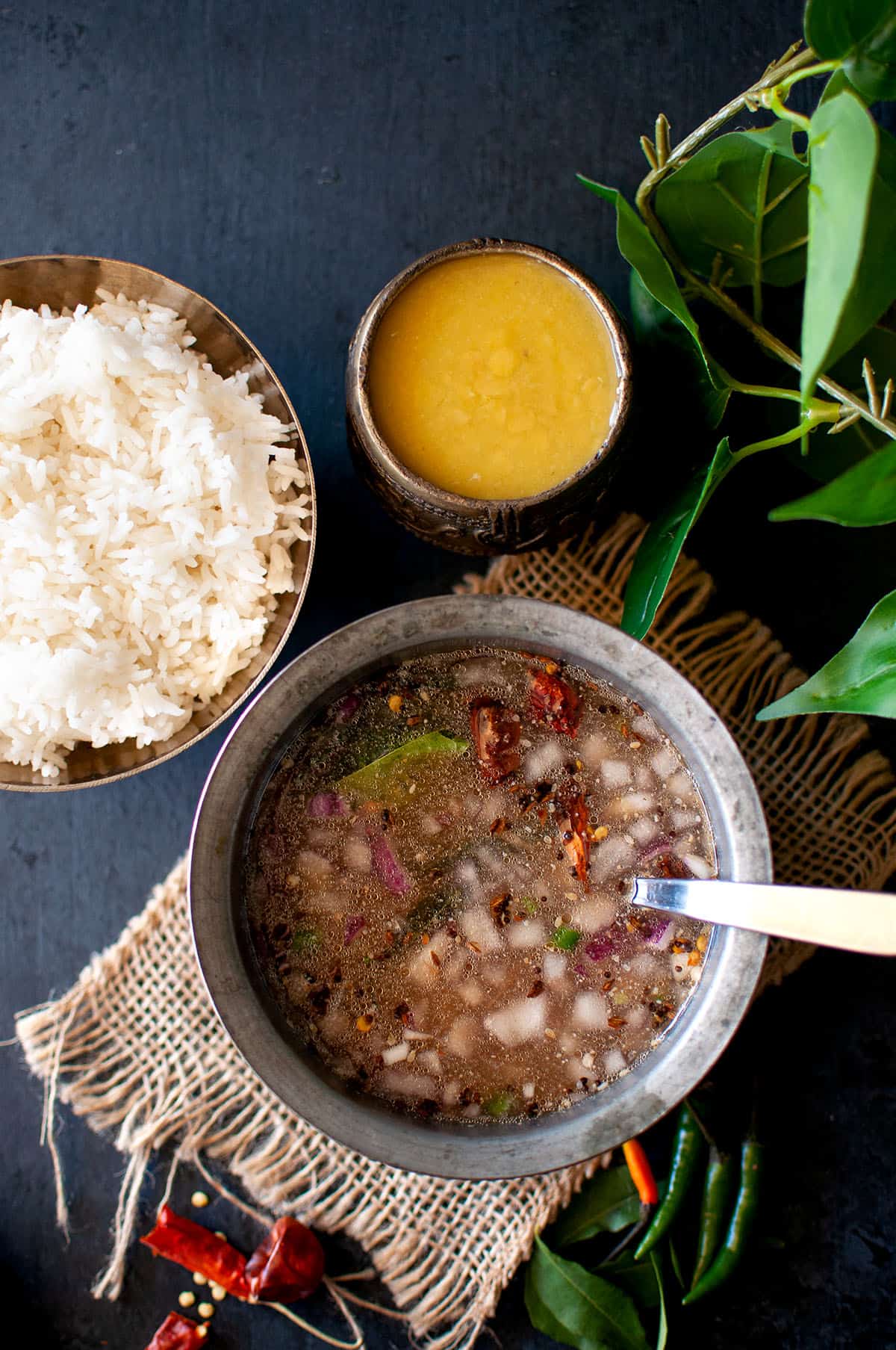 Bowl with tamarind onion stew and a bowl of rice in the back.