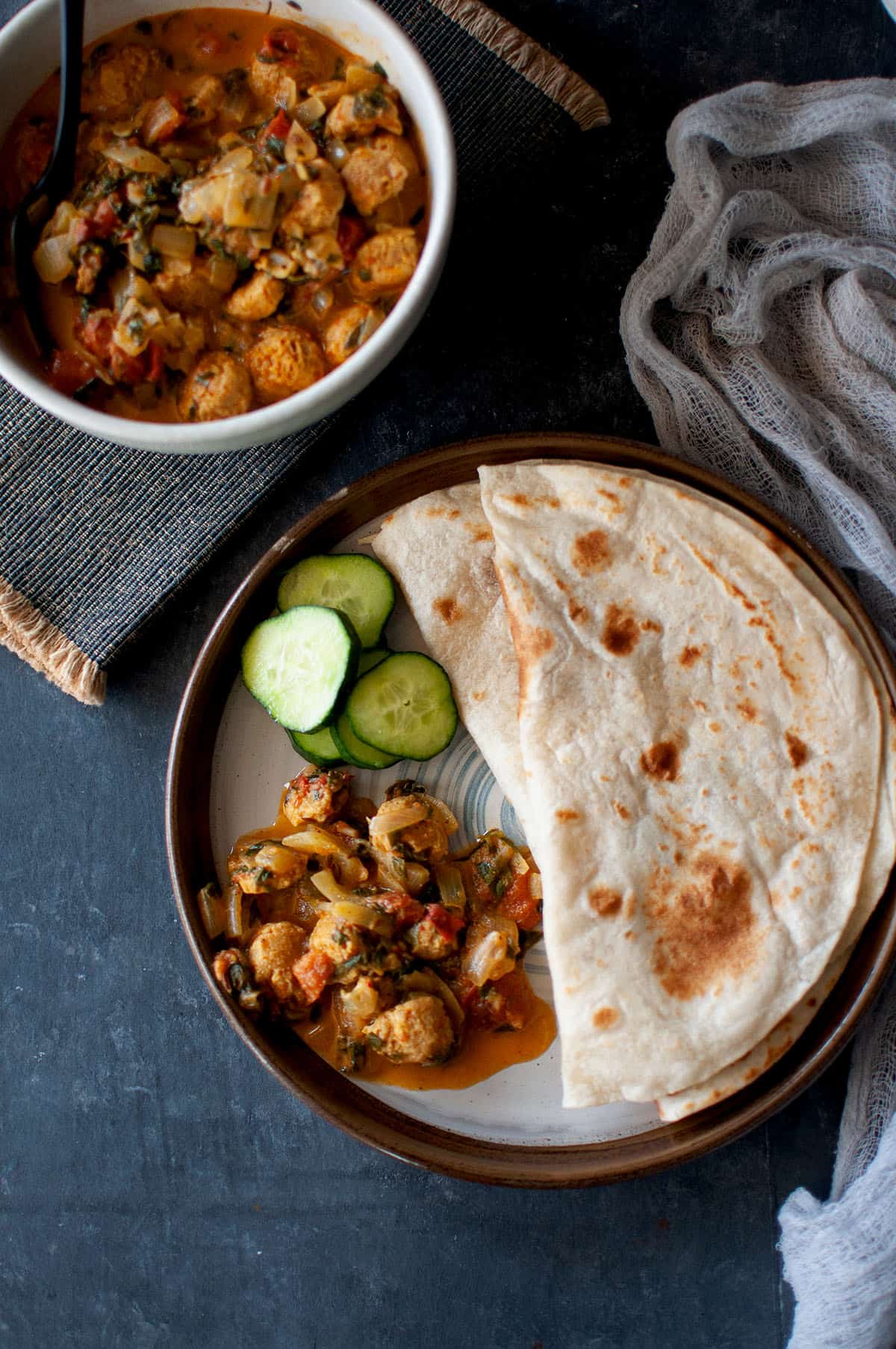 Brown plate with methi soya curry with roti and cucumber slices.