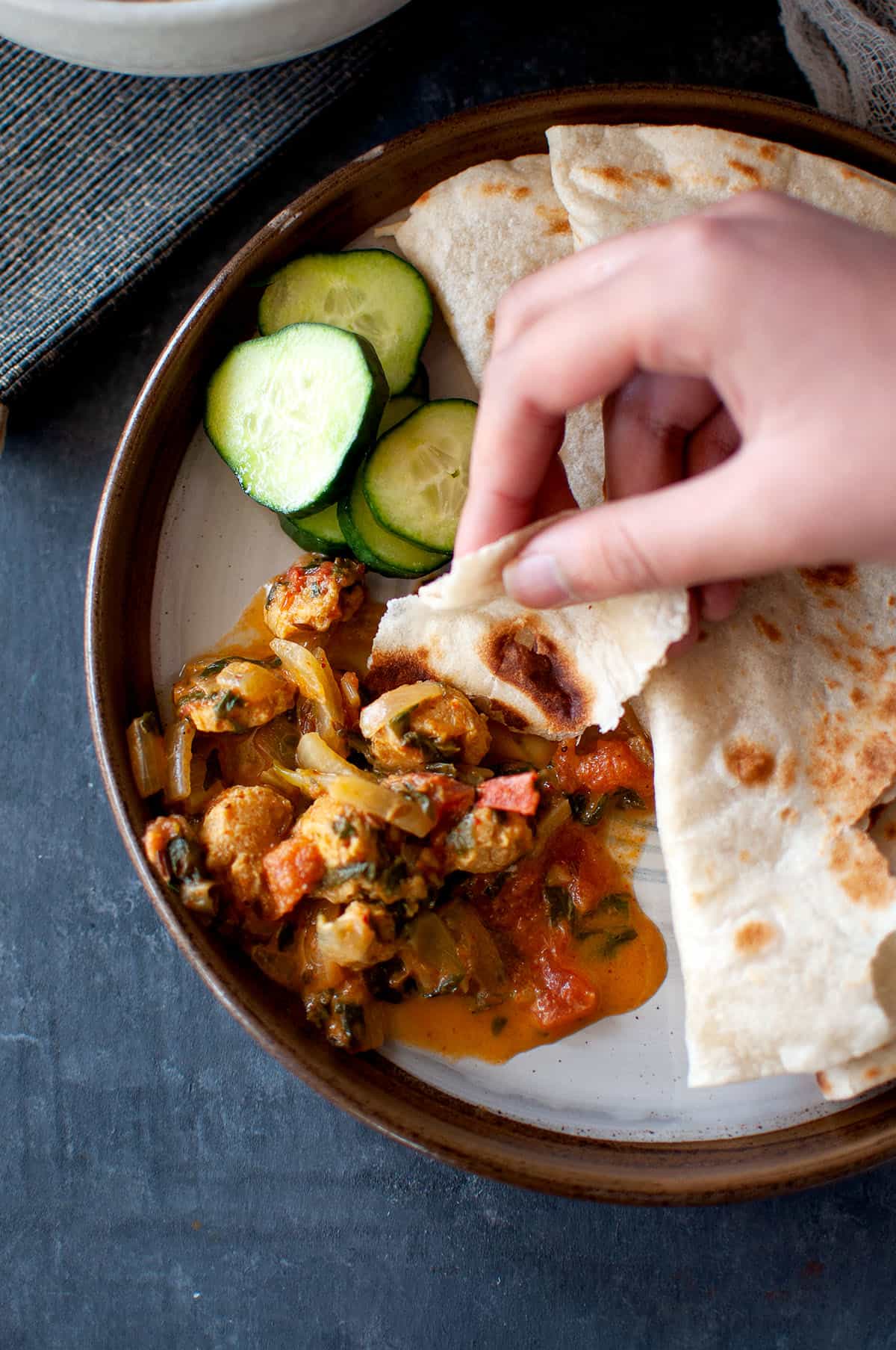 Hand picking up curry from a brown plate.