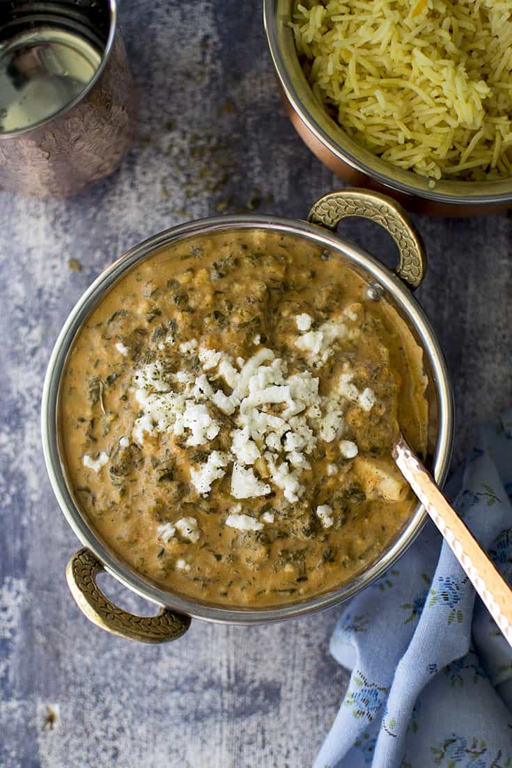 Steel bowl with curry topped with paneer and rice in the background