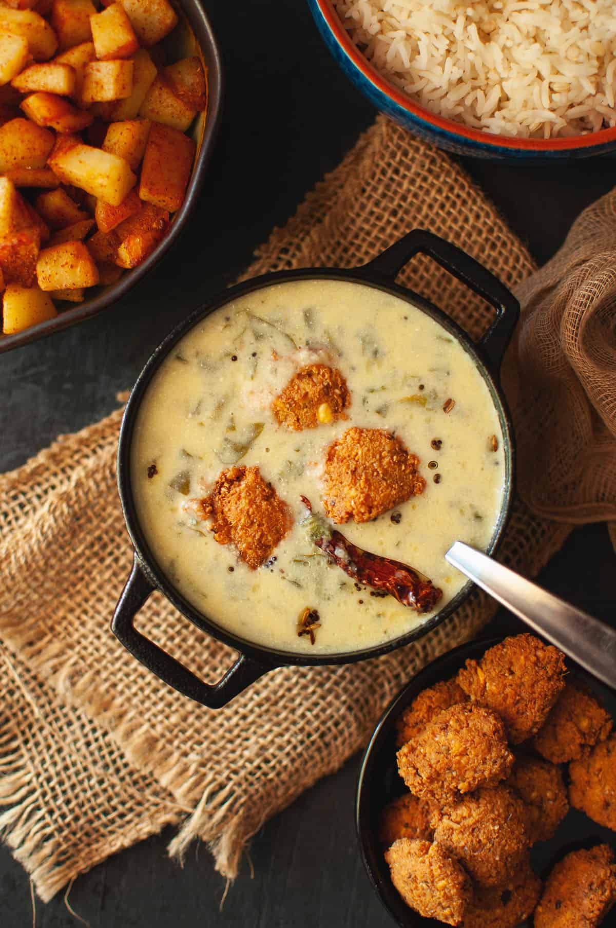 Black pan with mor kuzhambu topped with vada.