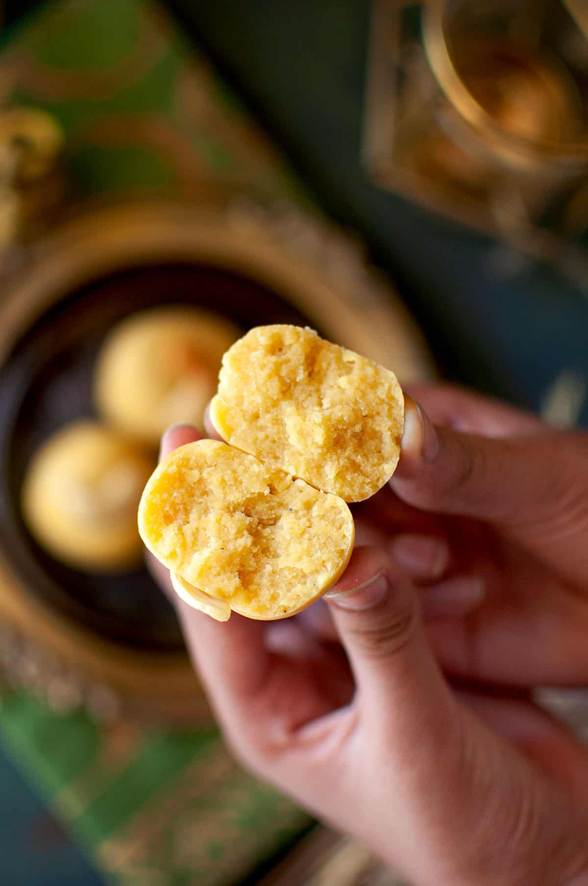 Hand holding a half of a besan ladoo.