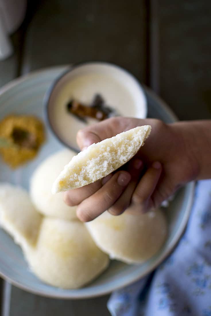 Hand holding half an Idli with chutney in the background