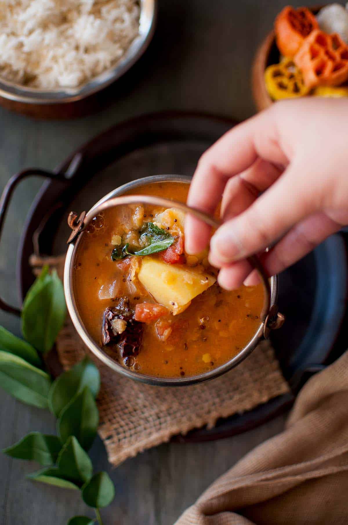 Hand holding a brass bucket with Slow cooker Sambar