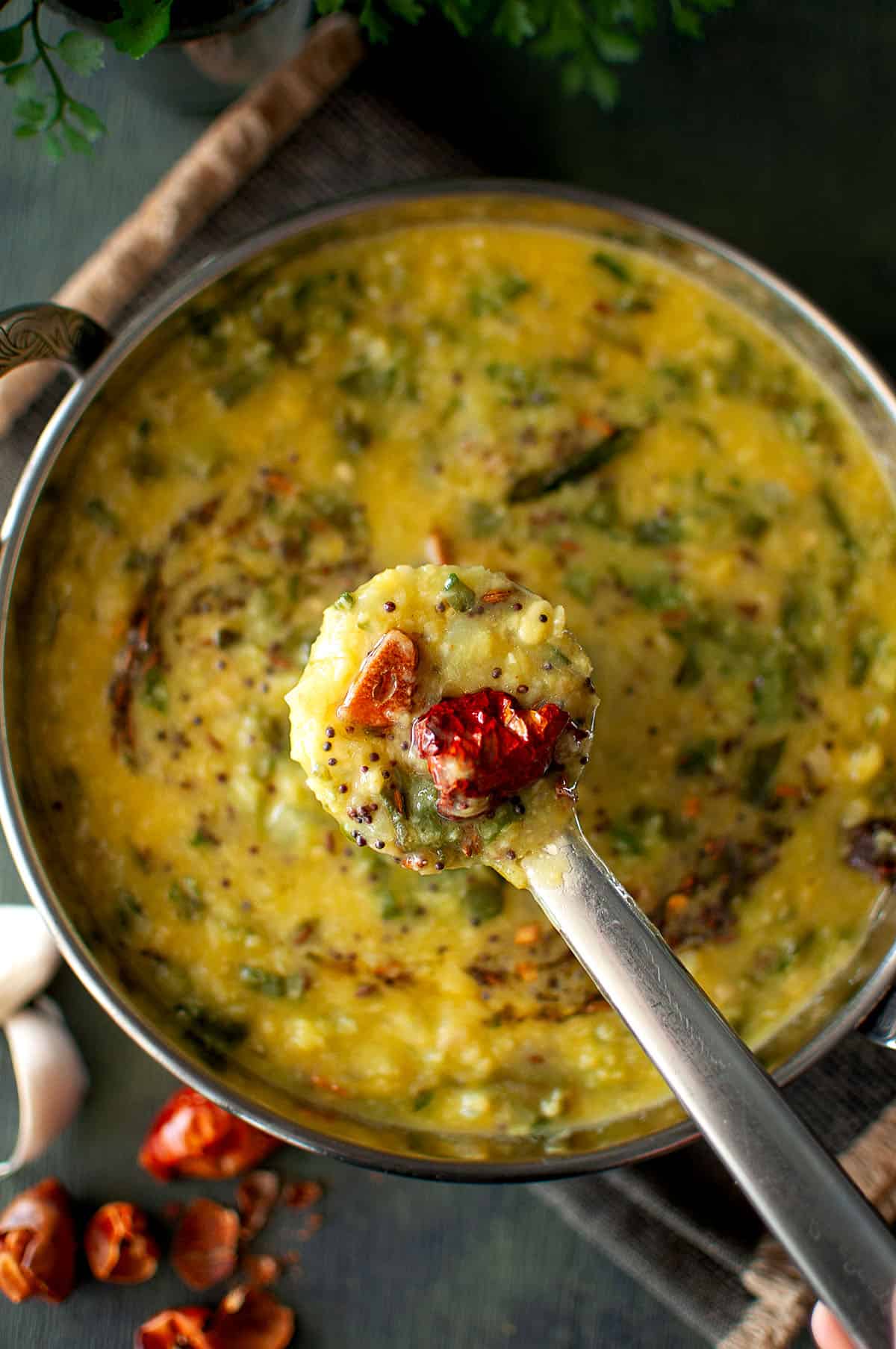 Steel ladle with palak dal over a bowl of pappu.