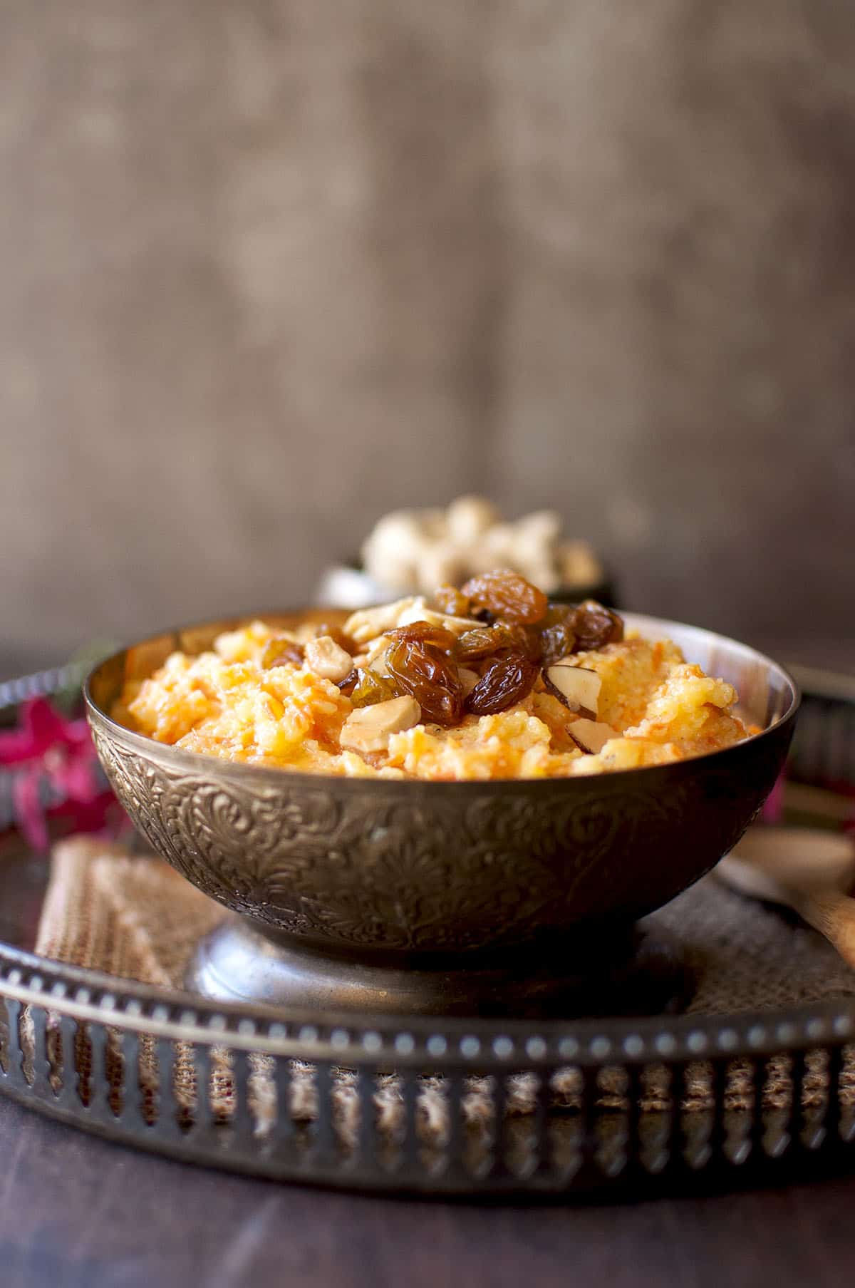 Brass bowl with carrot sooji halwa topped with raisins and cashews