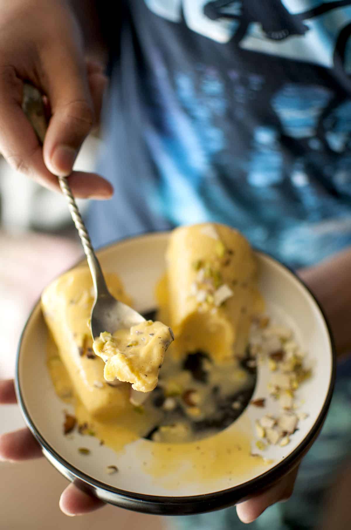 Hand holding a black & white bowl and spoon of mango kulfi