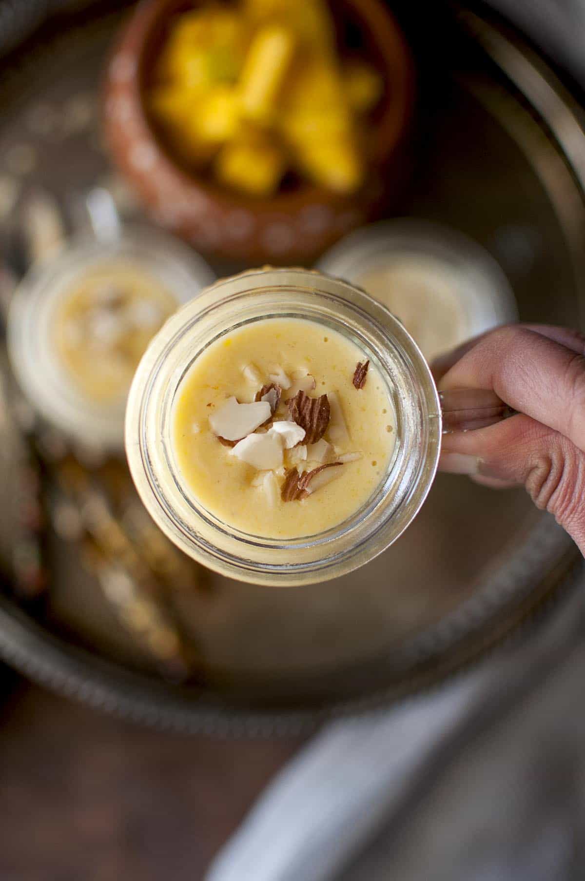 Hand holding a glass cup with Mango kheer