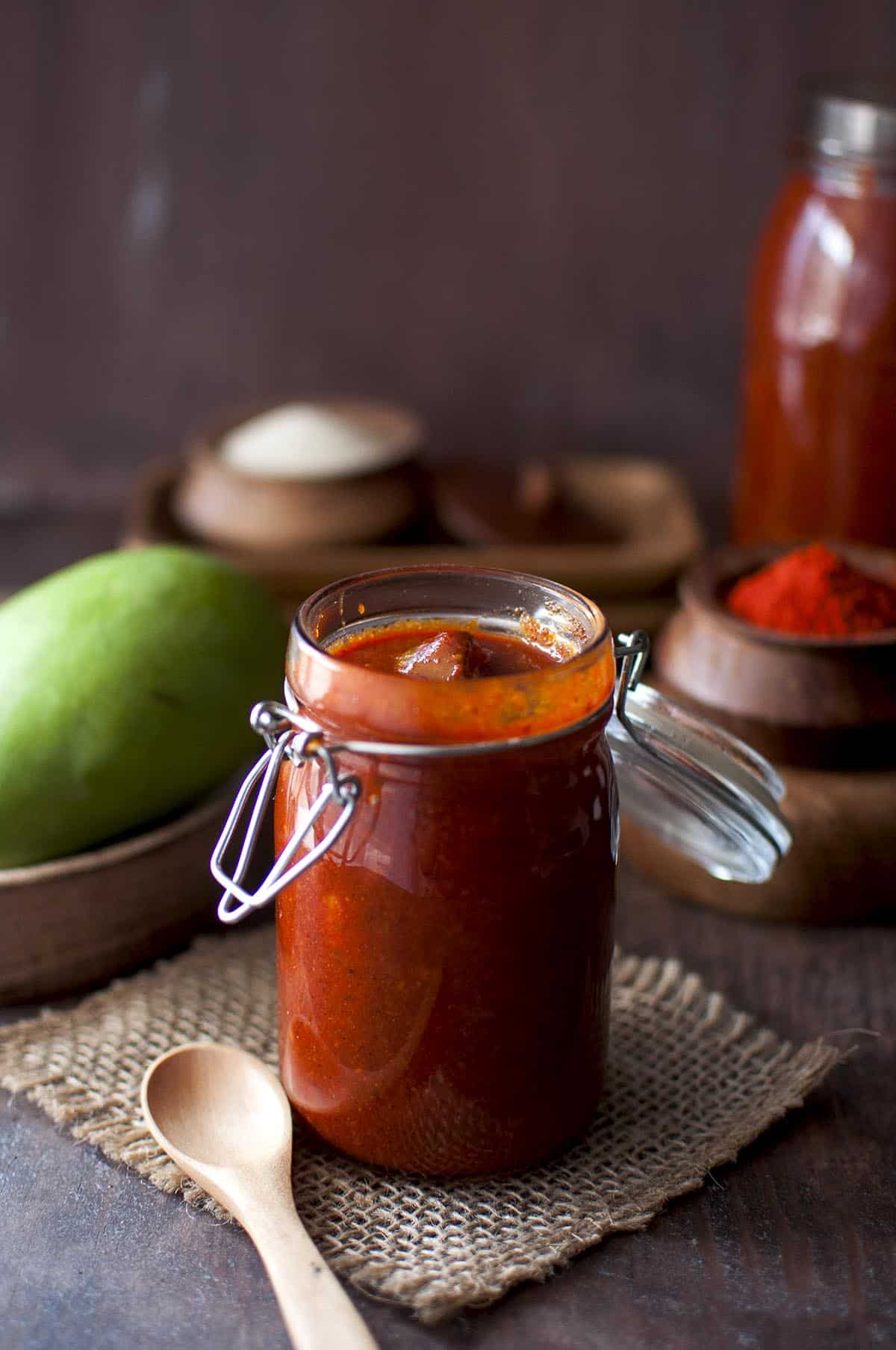 Glass bottle with sweet mango pickle and a wooden spoon next to it