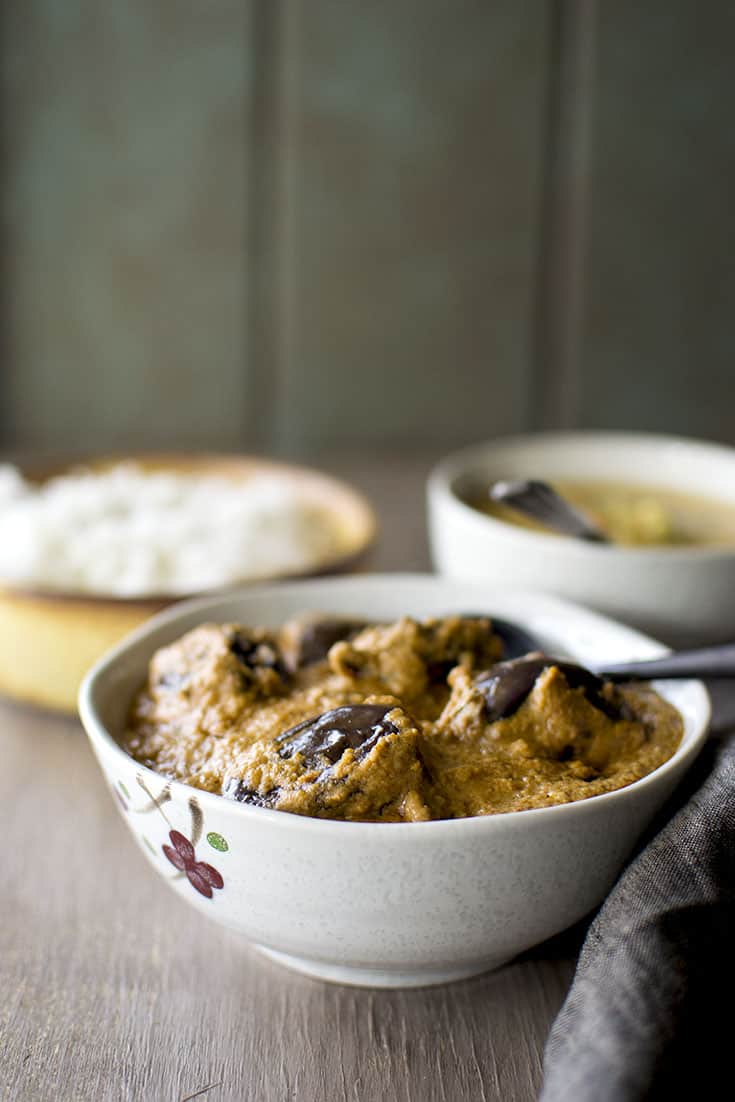 White bowl with stuffed eggplant curry with rice and dal in the background