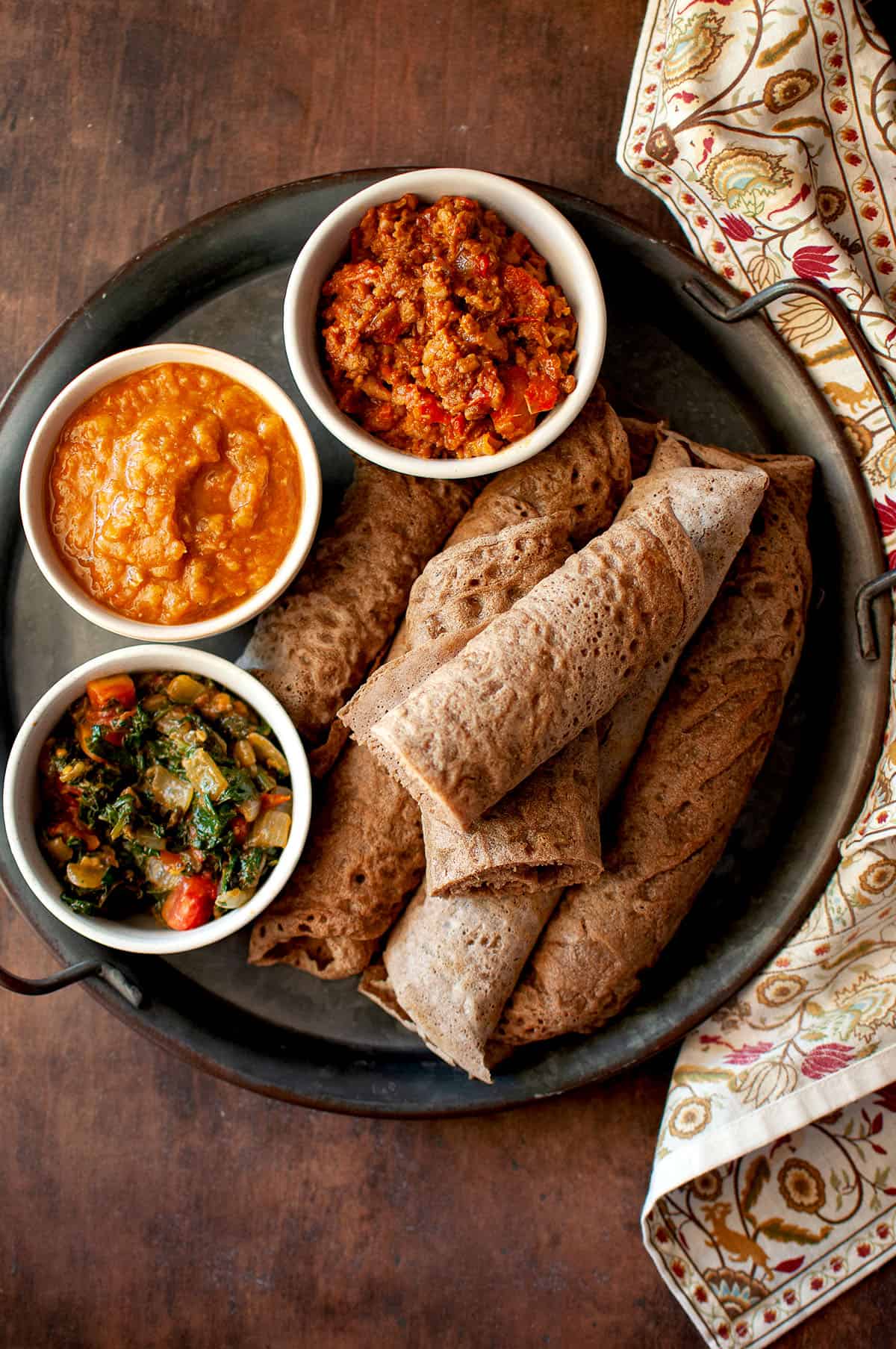 Tray with rolled Sourdough Injera and bowls of side dishes.