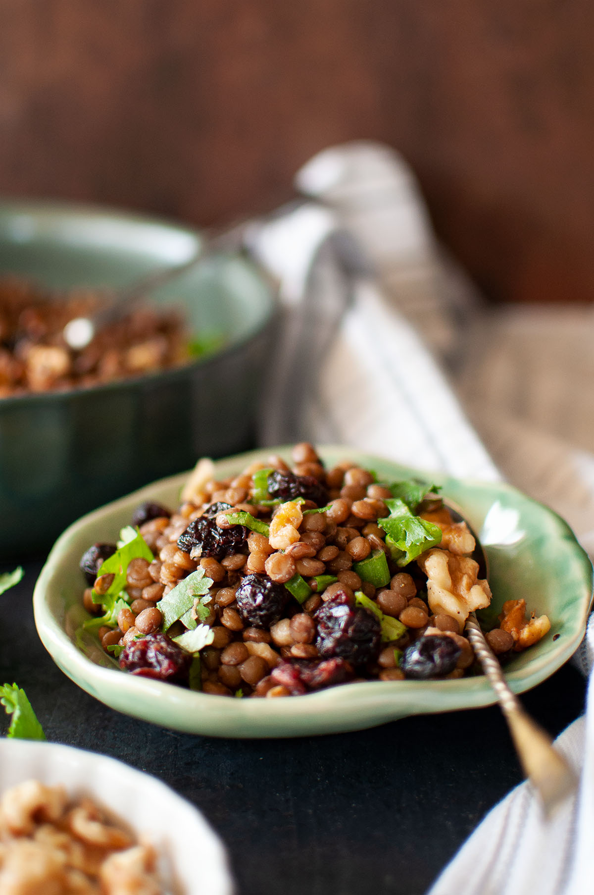 green plate with warm lentil salad topped with walnuts & berries.