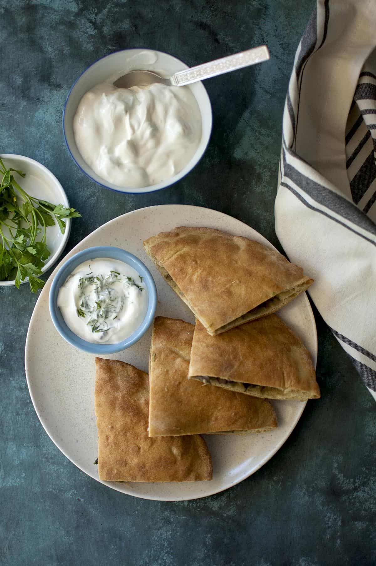 White plate with wedges of onion kulcha and bowl of raita