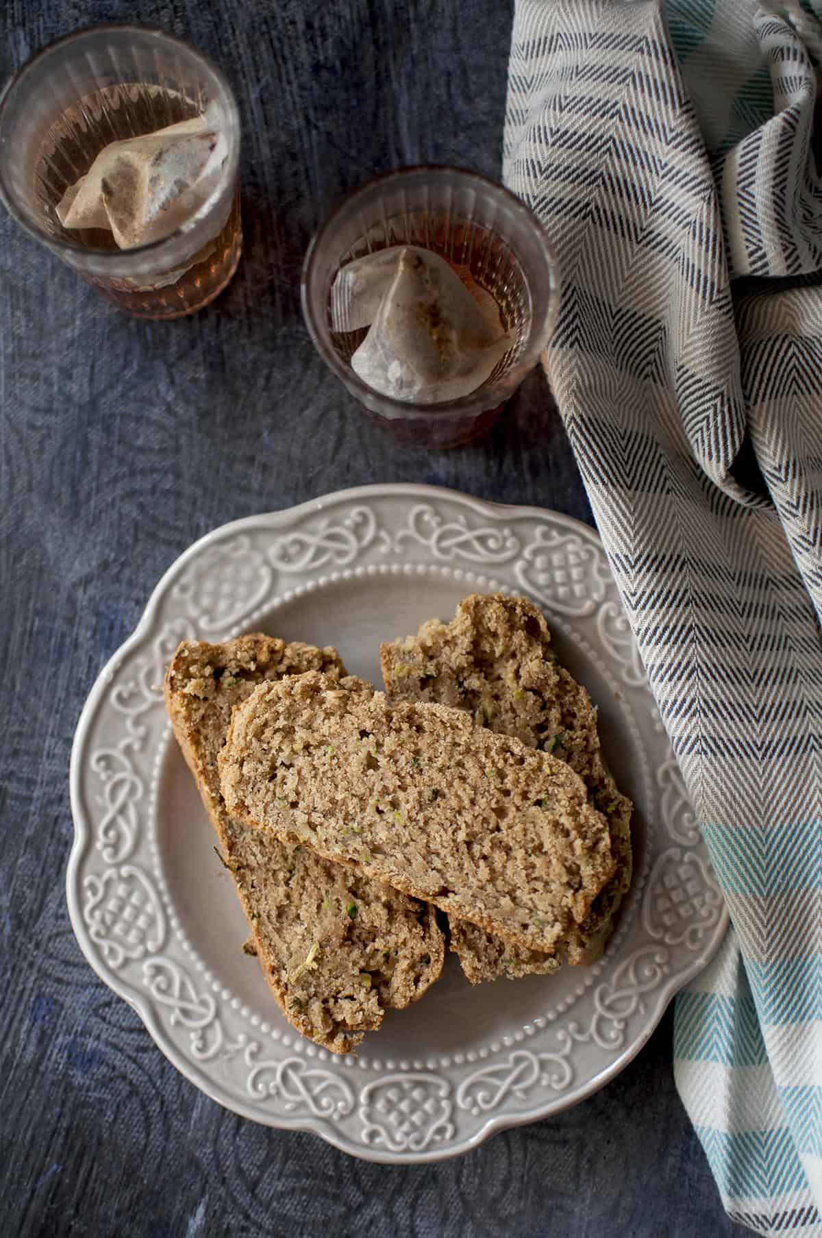 grey plate with slices of zucchini sourdough bread and 2 cups of tea in the background