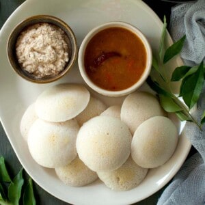 White tray with parboiled rice idli with bowls of sambar and peanut chutney