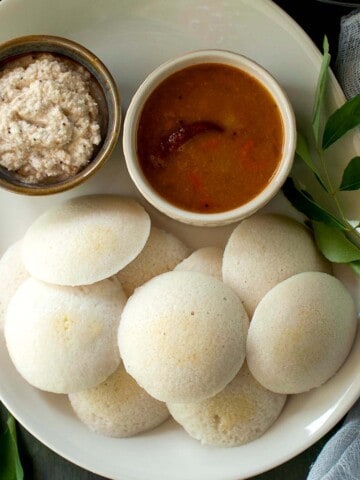 White tray with parboiled rice idli with bowls of sambar and peanut chutney