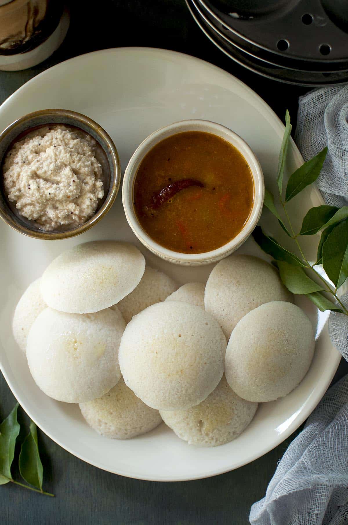 White tray with parboiled rice idli with bowls of sambar and peanut chutney