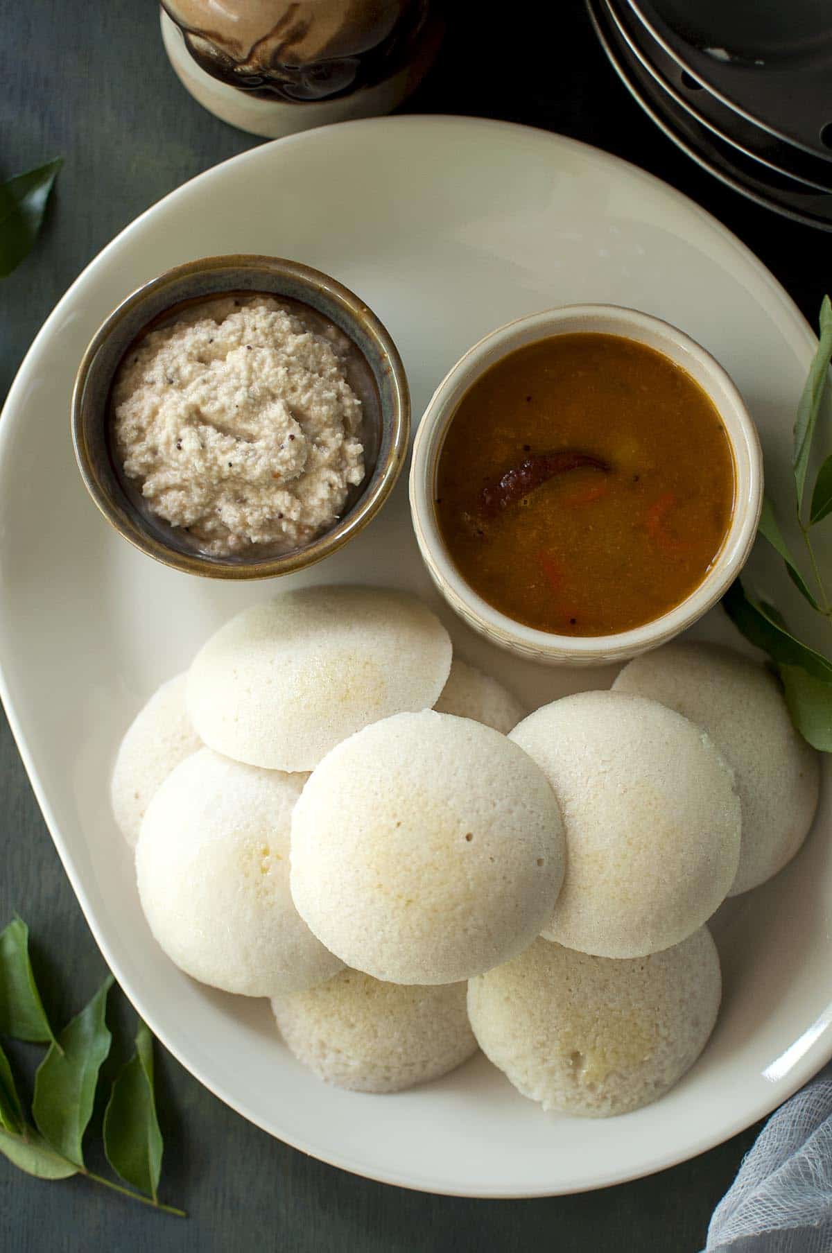 White tray with parboiled rice idli with bowls of sambar and peanut chutney