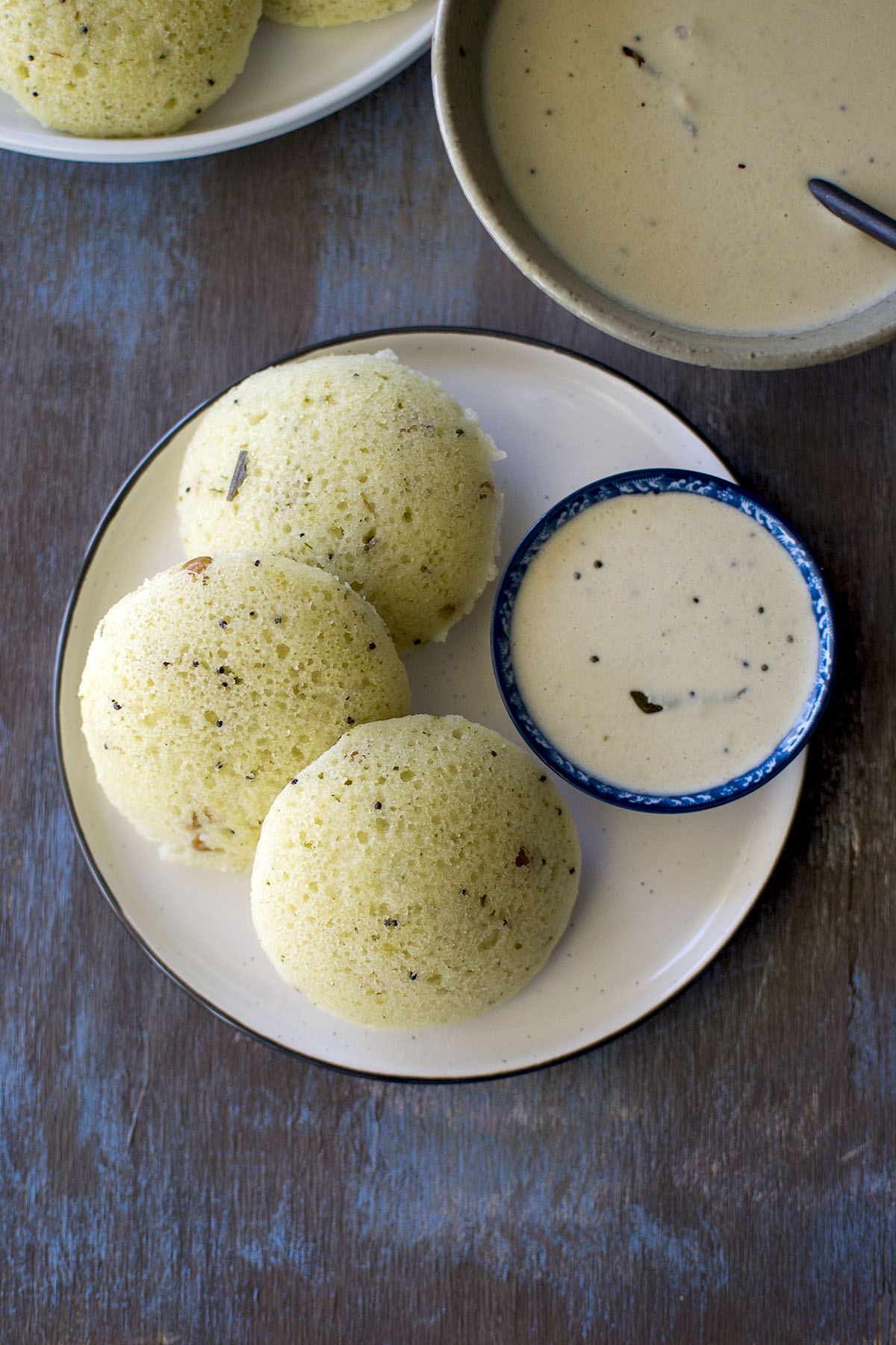 White plate with 3 steamed idli and a bowl of chutney