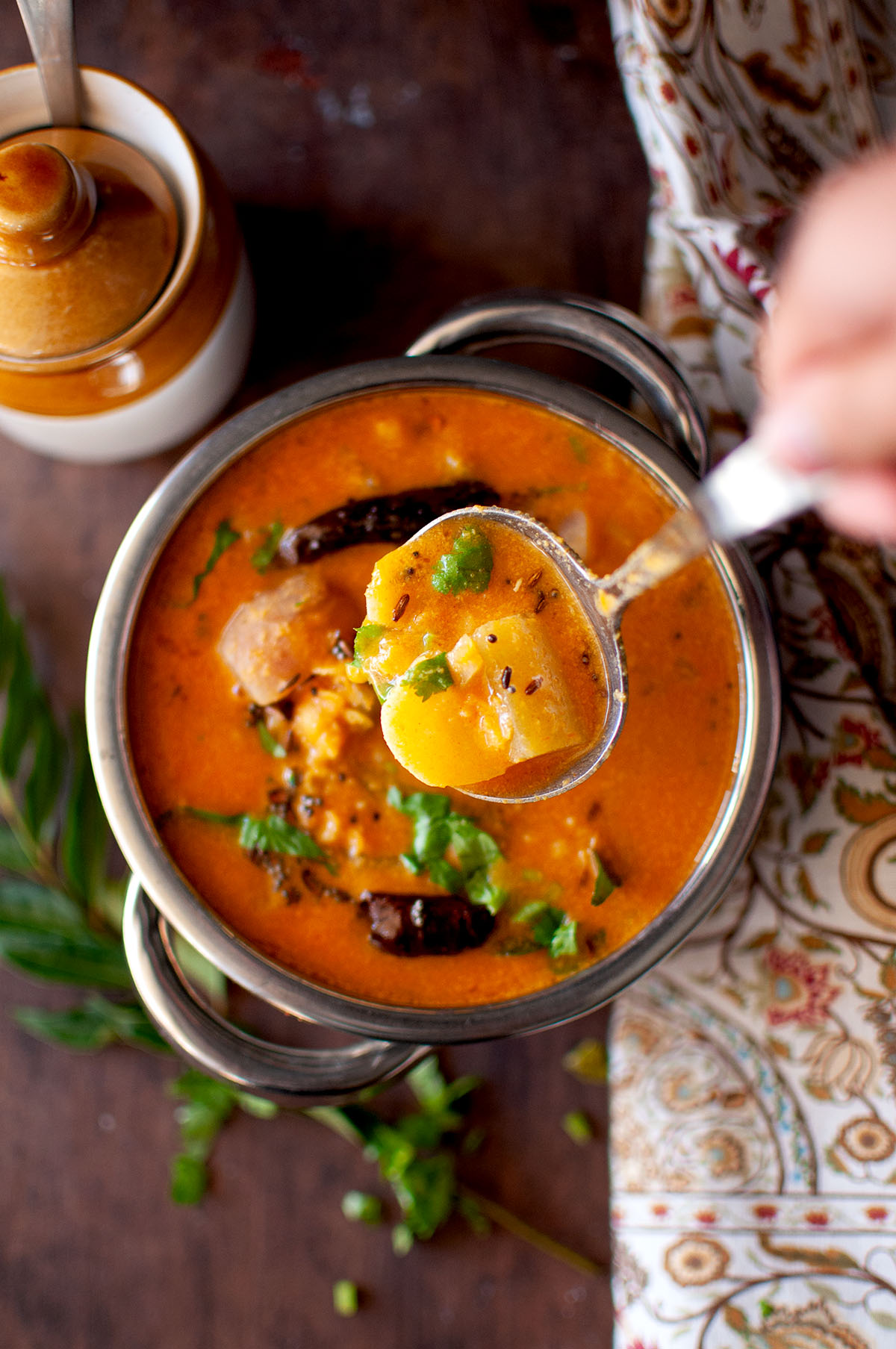 Hand holding a ladle with instant pot sambar.