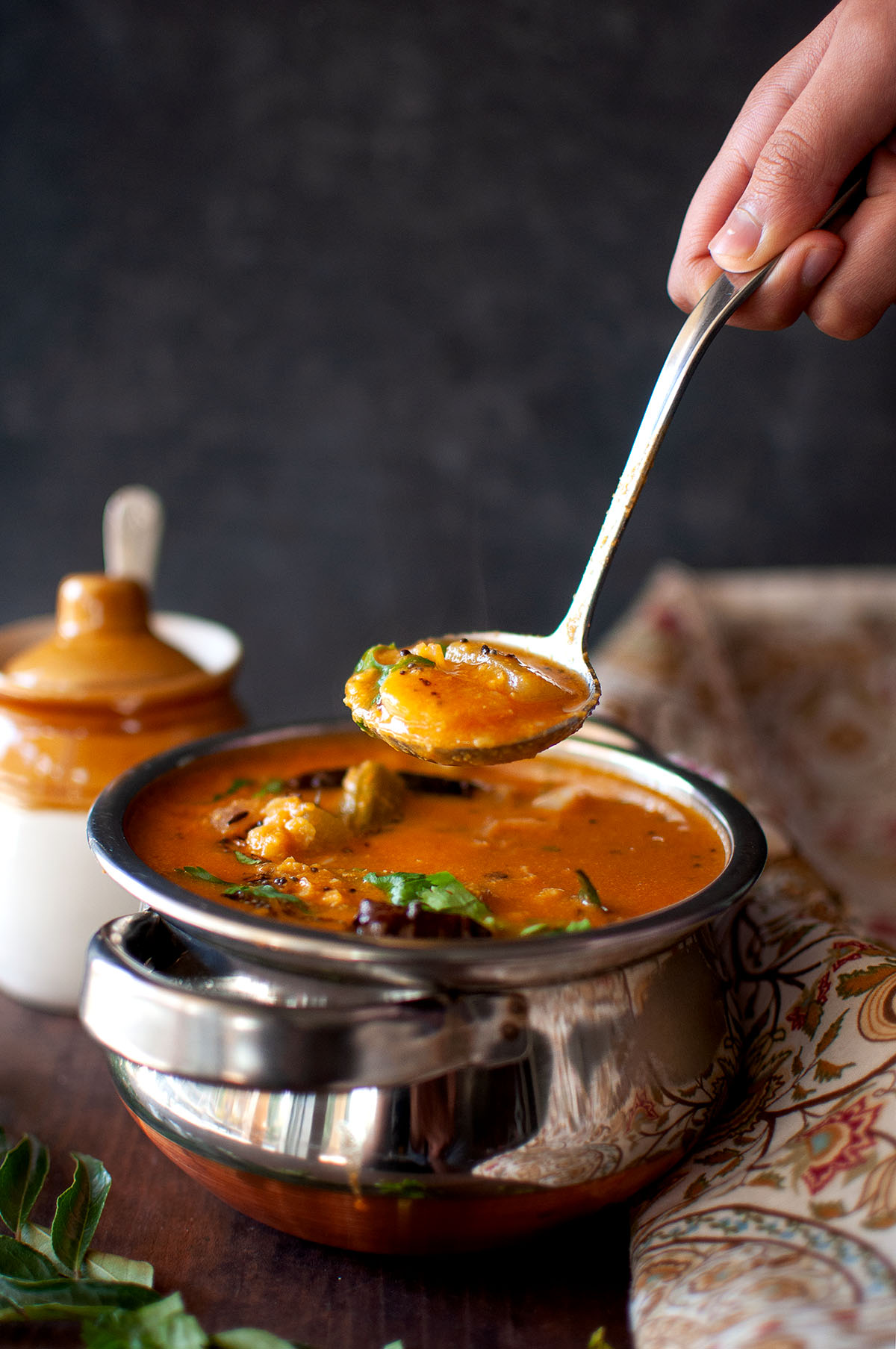 Hand holding a ladle with masoor dal sambar.