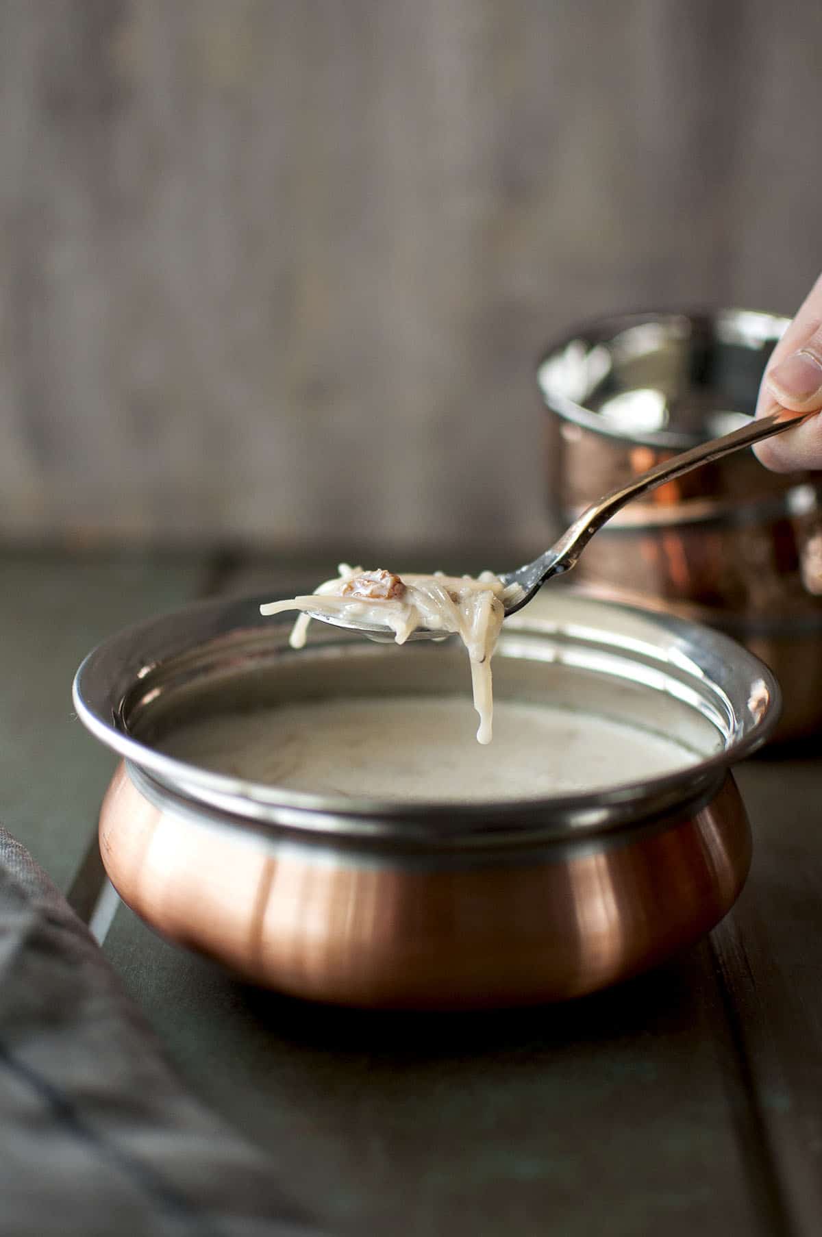 Copper bowl with vegan kheer and a hand holding a spoon