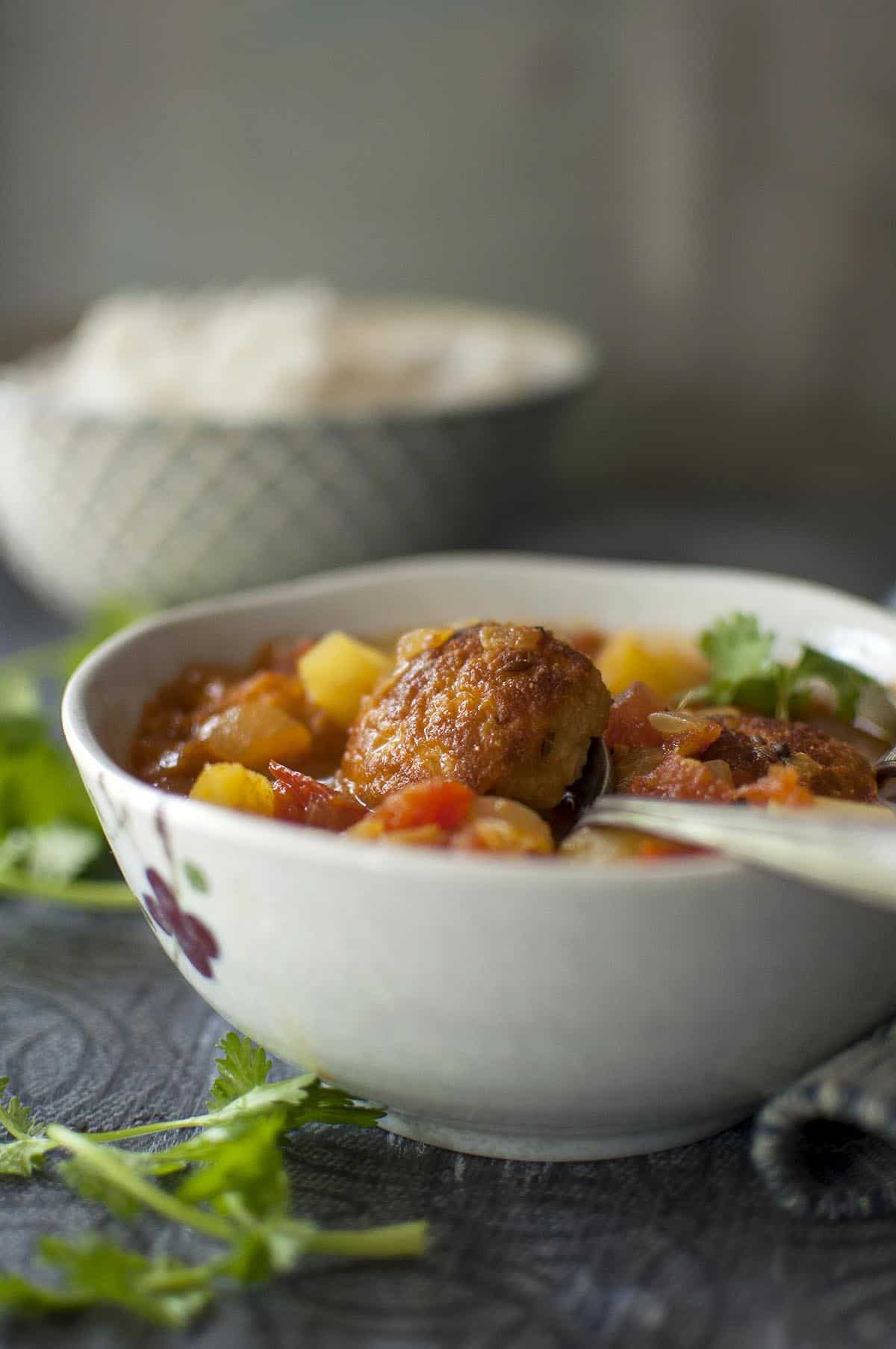 Grey bowl with Bengali fritter curry and a spoon inside