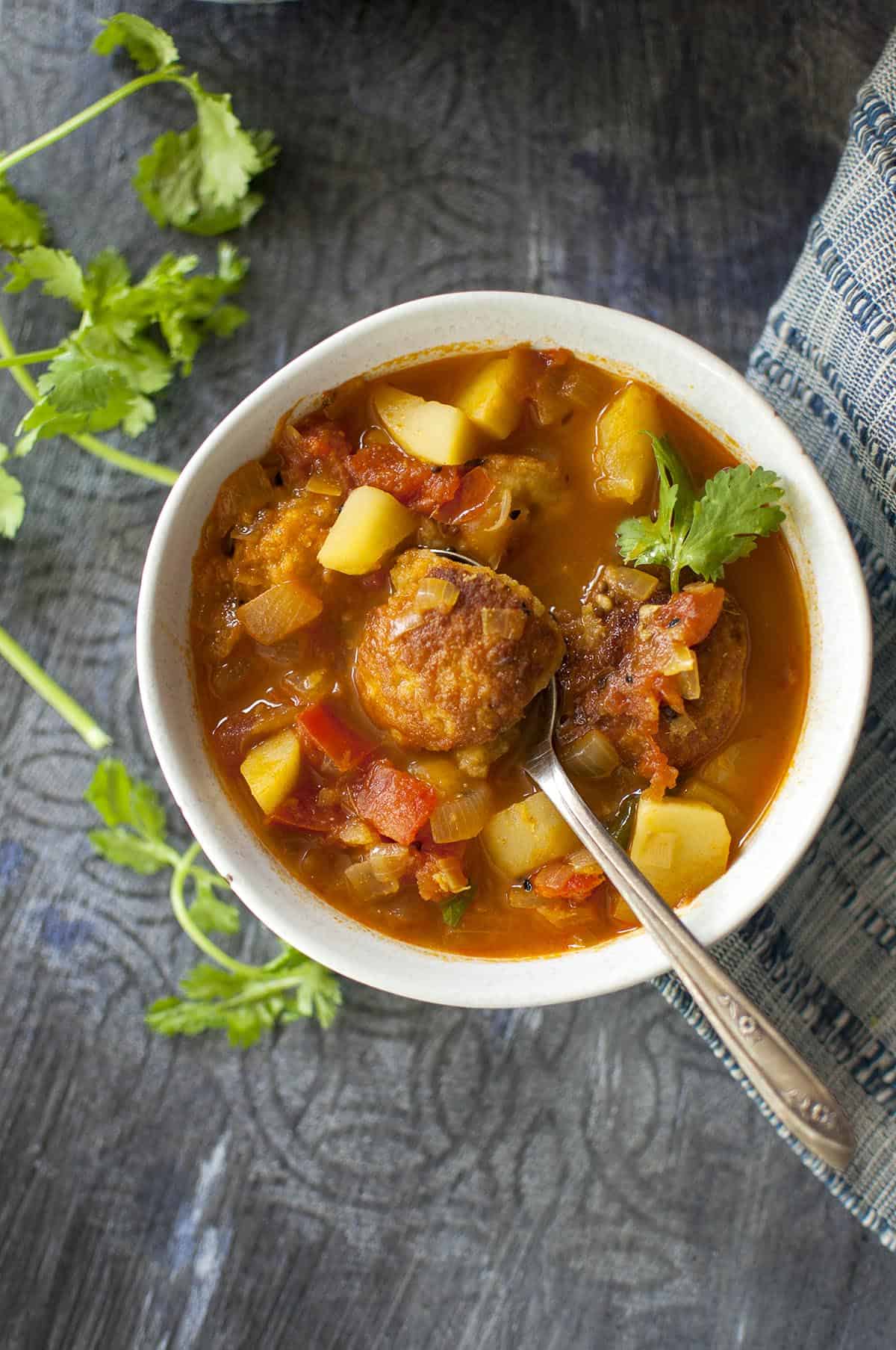 White bowl with daler borar jhol with a spoon holding lentil fritter