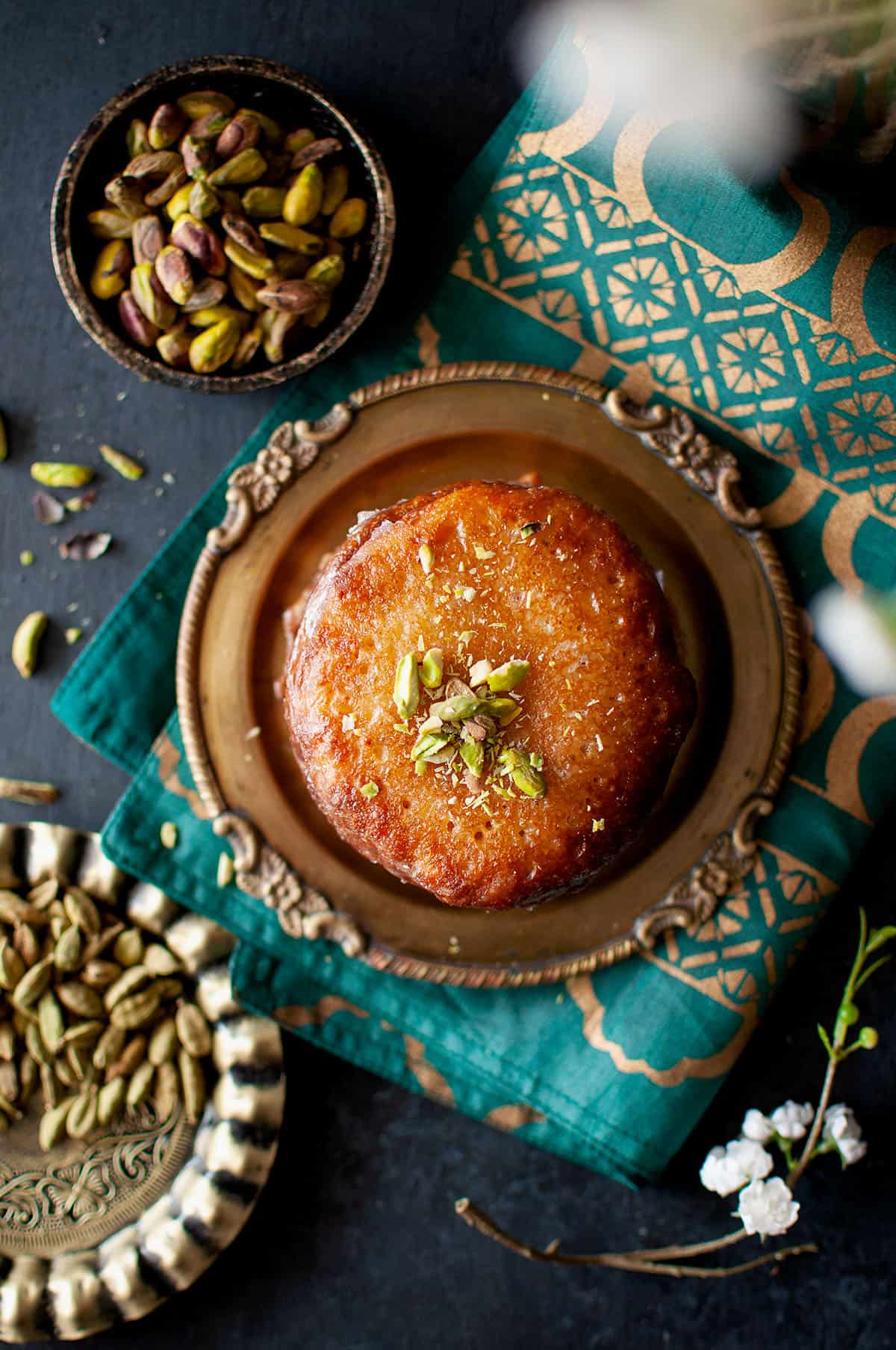 Brass plate with a stack of Bengali malpua topped with chopped pistachios.