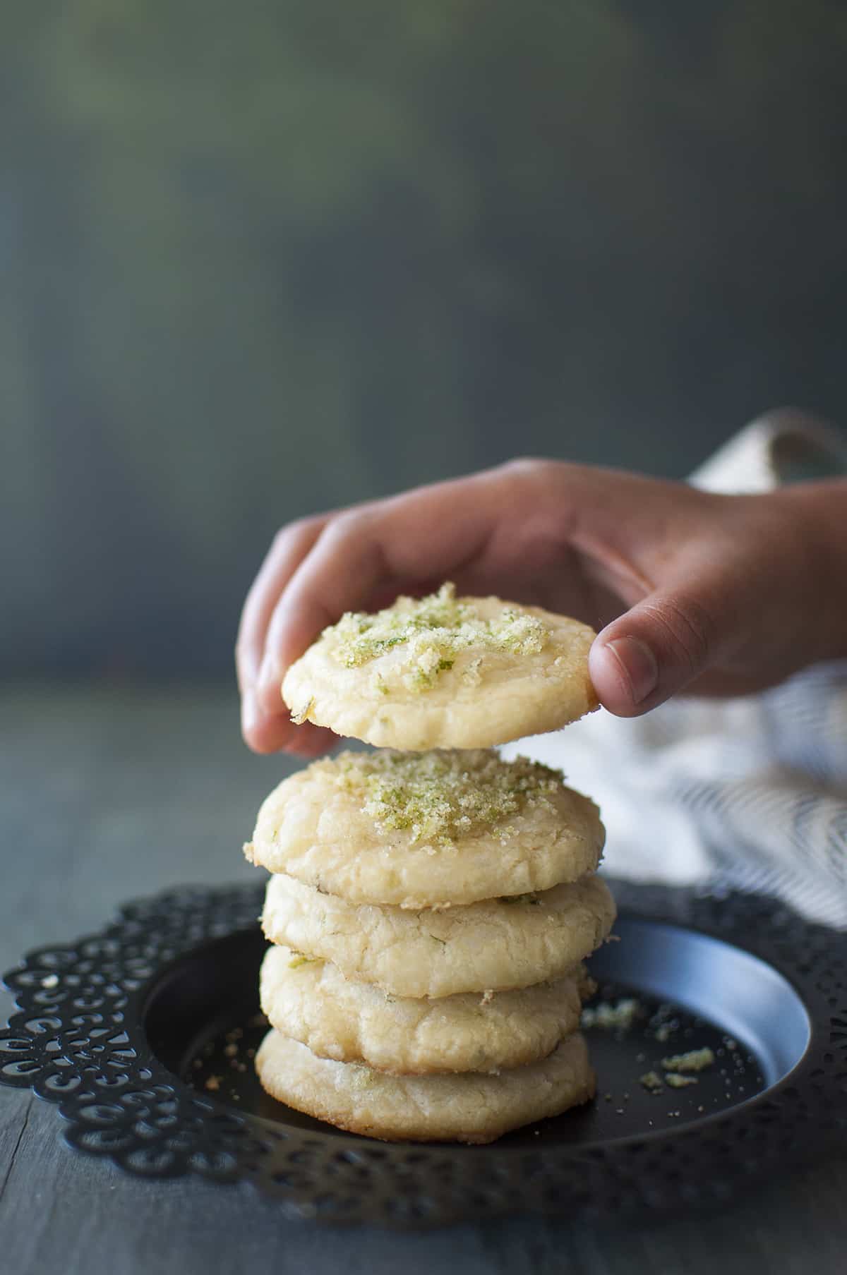 Black plate with a stack of lime cookies and a hand holding a cookie up