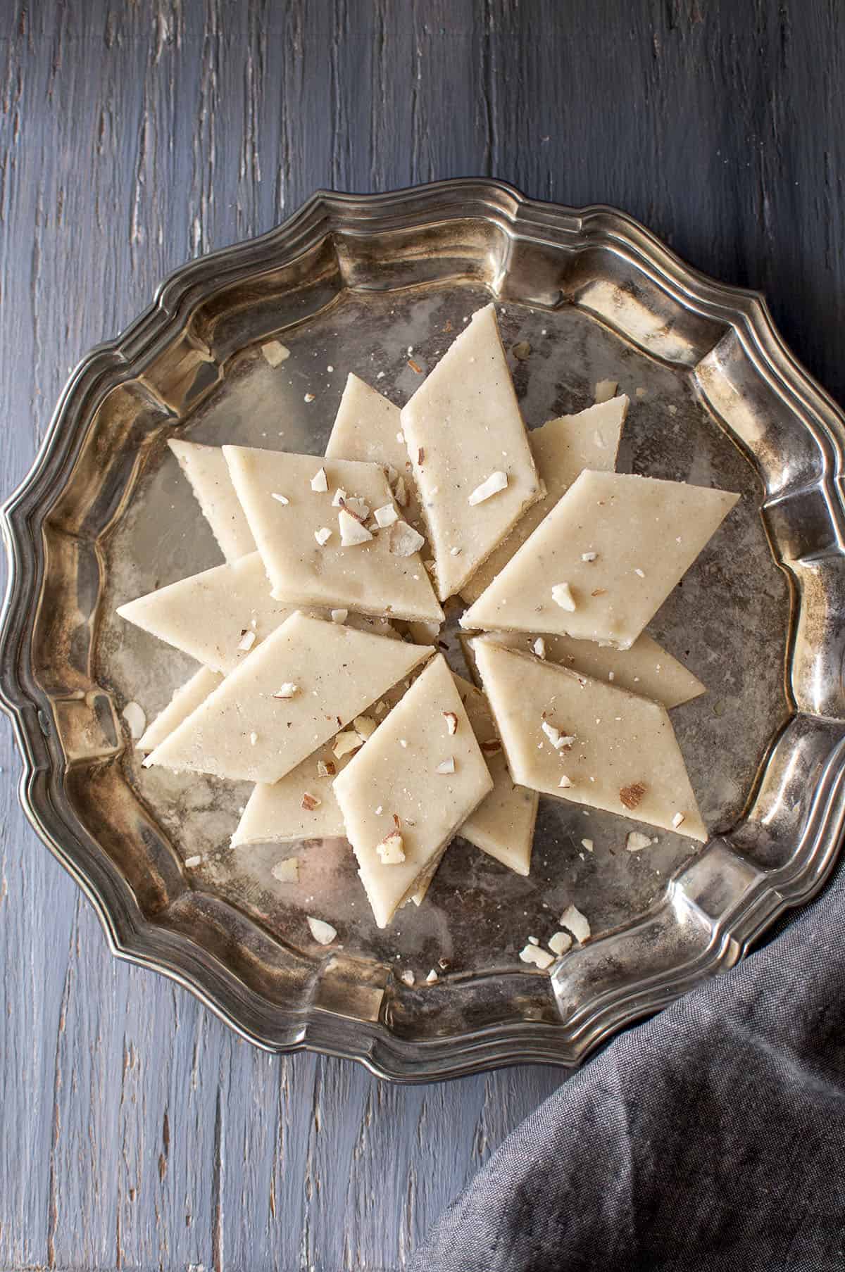 Pewter plate with kaju badam katli layered in a circle and sprinkled with chopped almonds