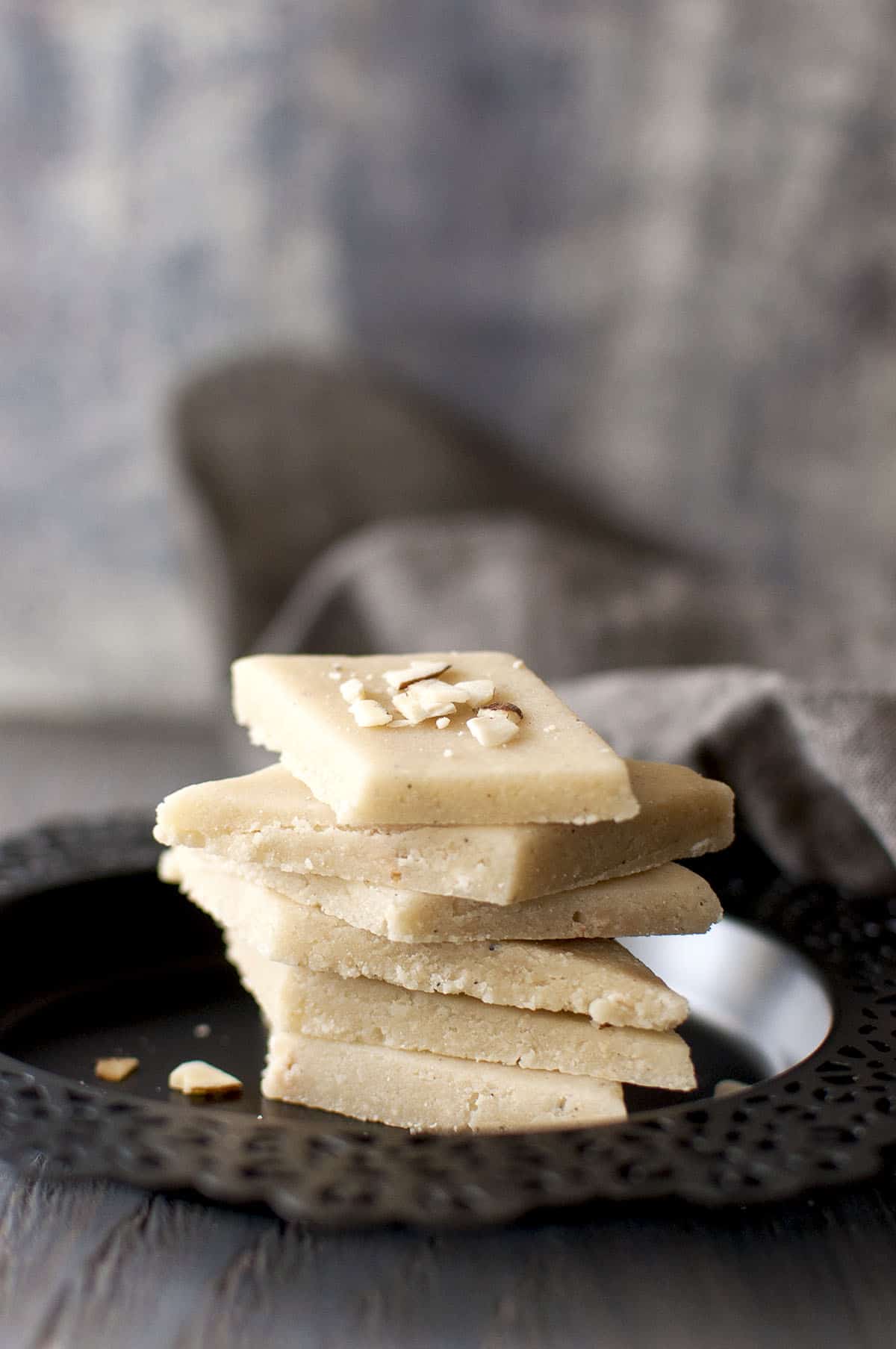 Black plate with a stack of burfi topped with chopped almonds