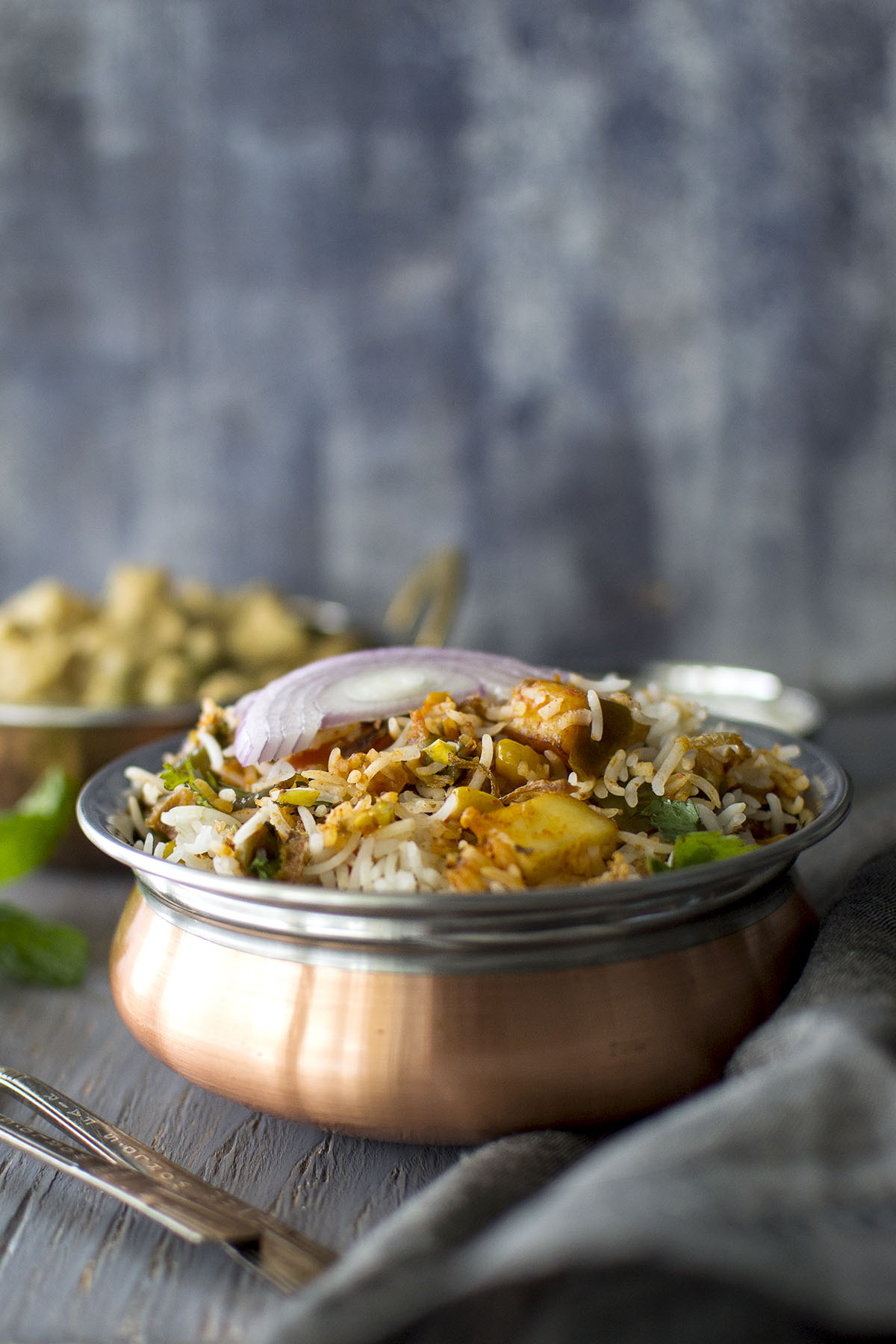 Copper bowl with Vegetable dum biryani topped with sliced red onion