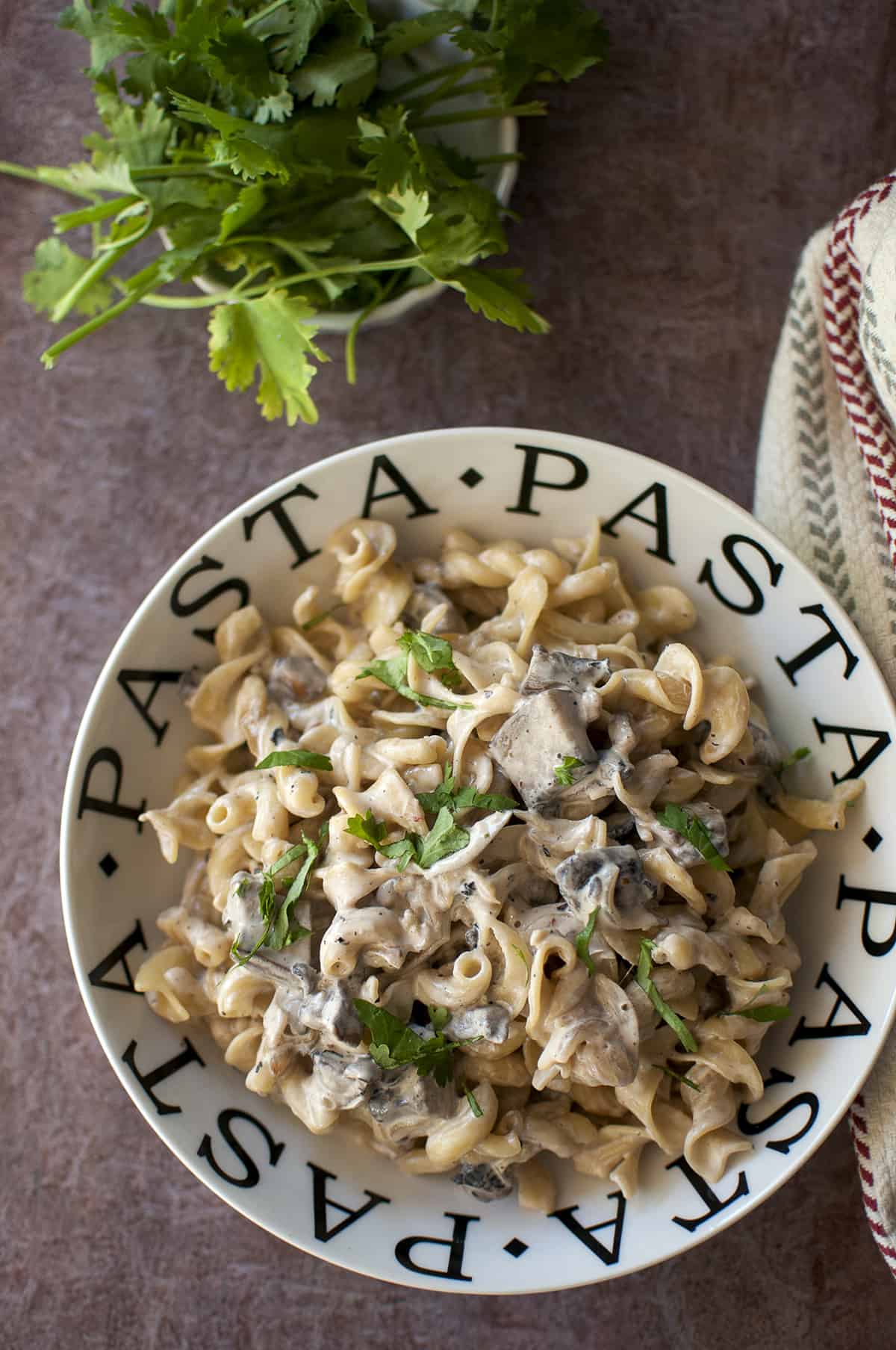 White bowl with mushroom pasta garnished with chopped cilantro