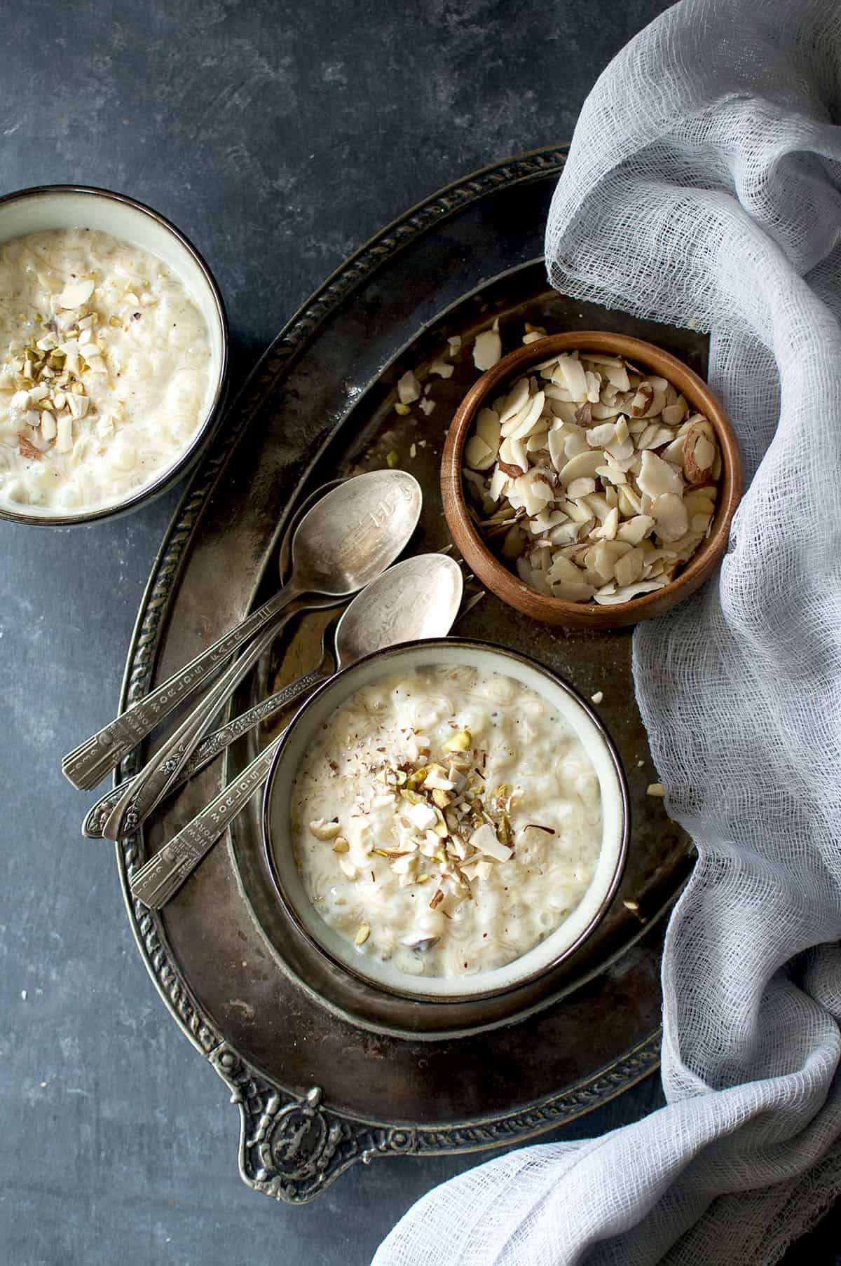 Grey bowl placed on a Pewter tray with sago kheer topped with nuts 