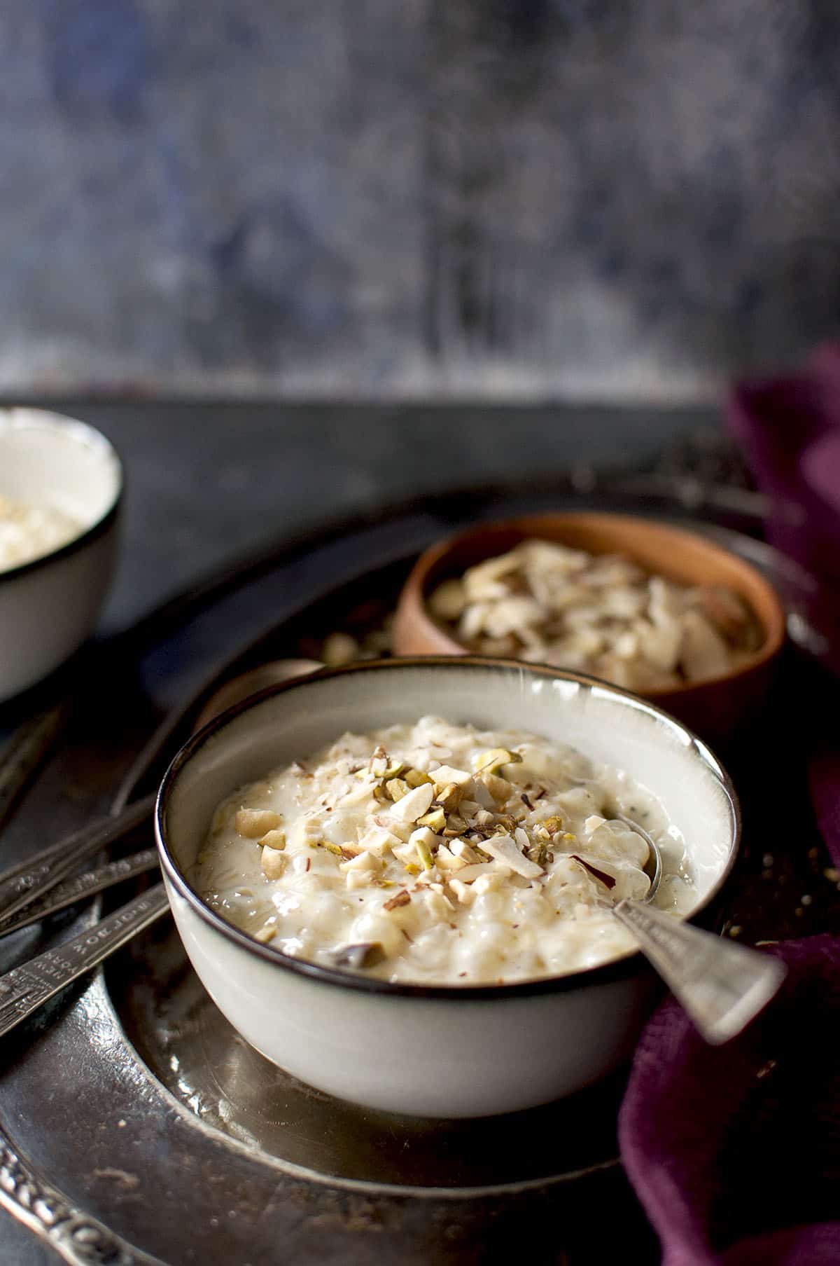 Grey bowl with tapioca pudding topped with chopped nuts and a spoon