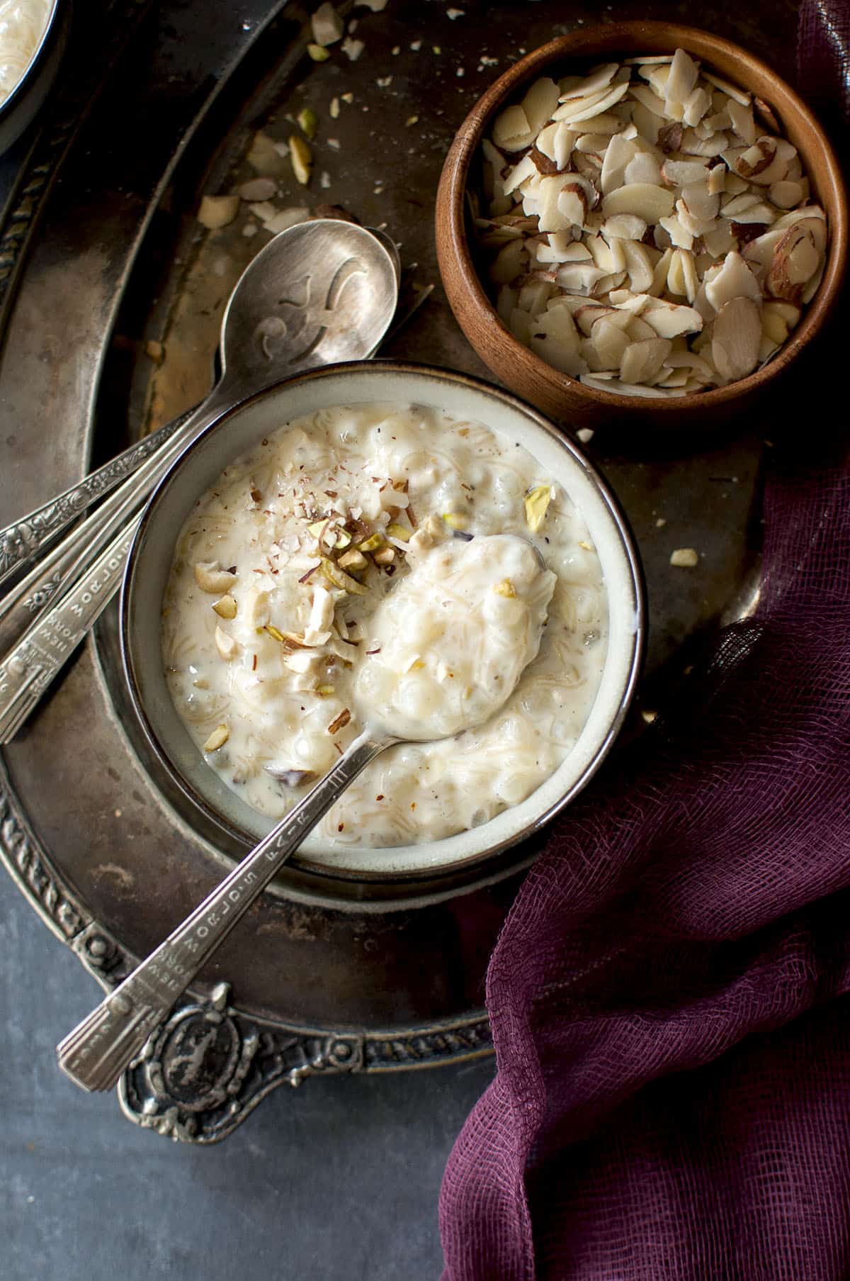 Grey bowl placed on a Pewter tray with sago kheer topped with nuts 