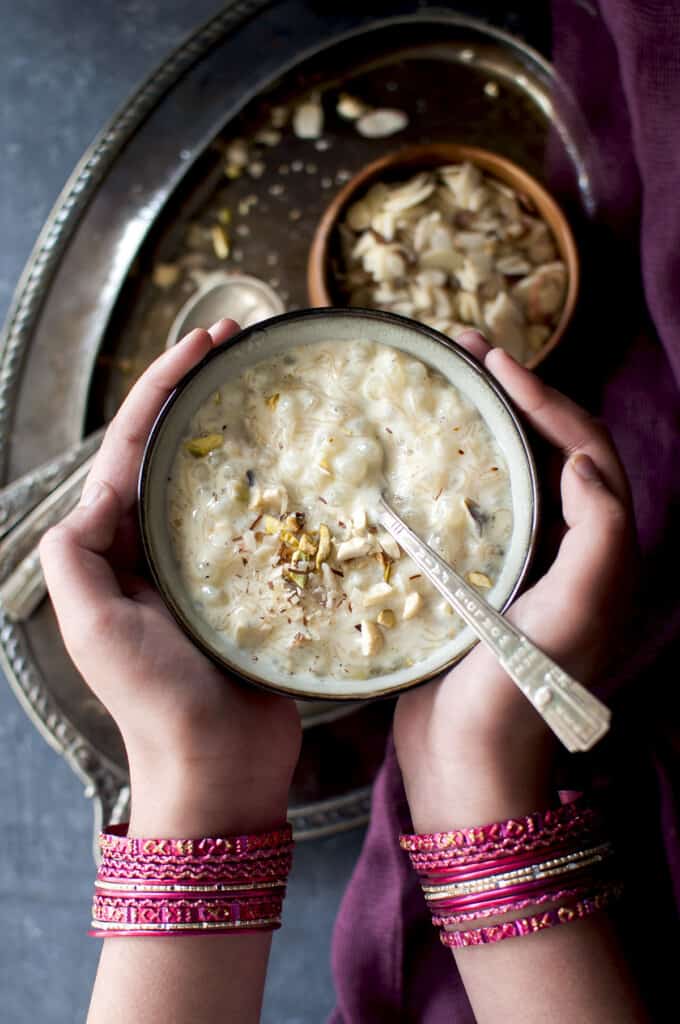Hands with pink bangles holding a grey bowl with Sindhi Kheerni