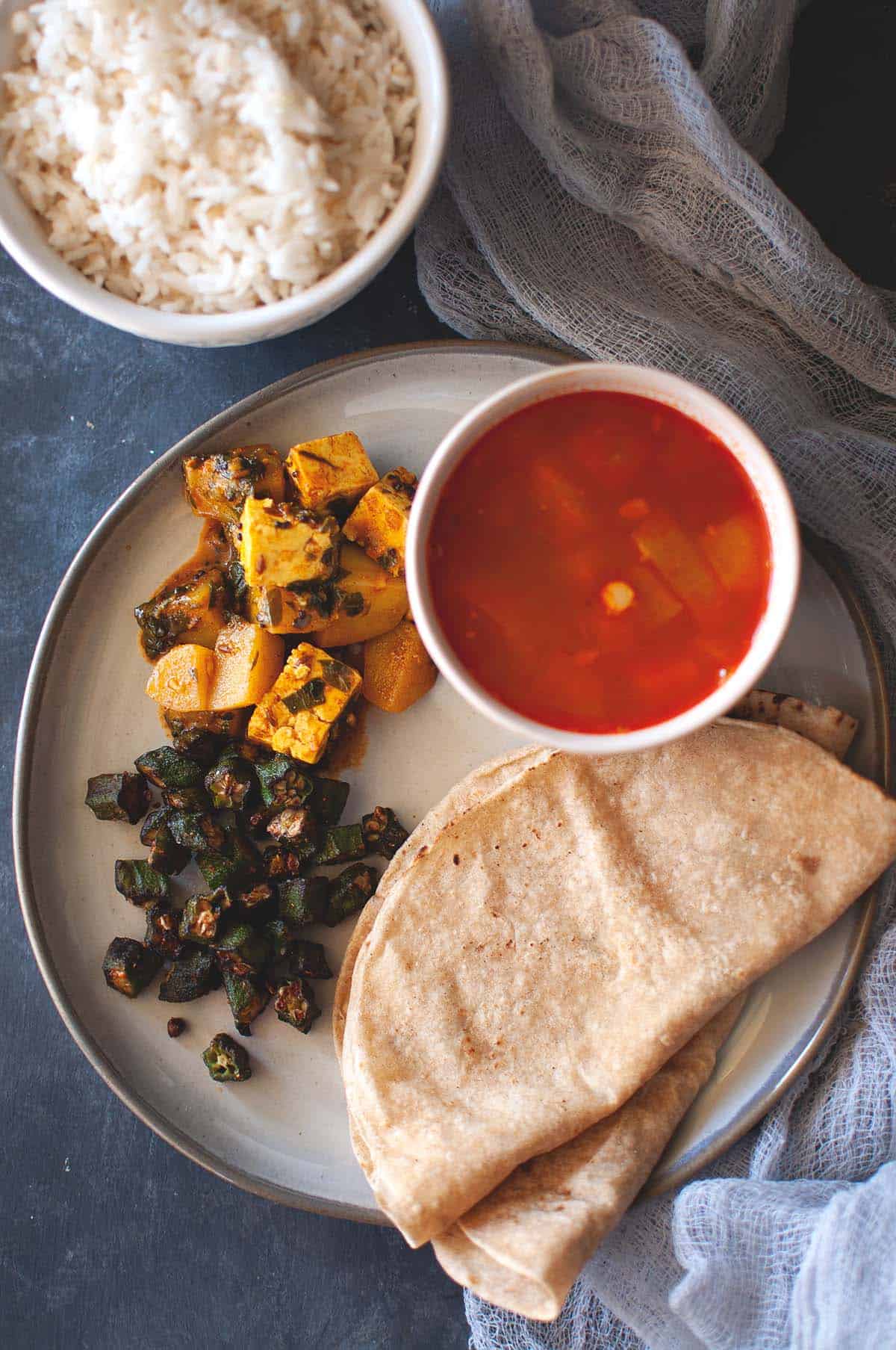 Grey plate with roti, okra curry, paneer curry and dalcha.