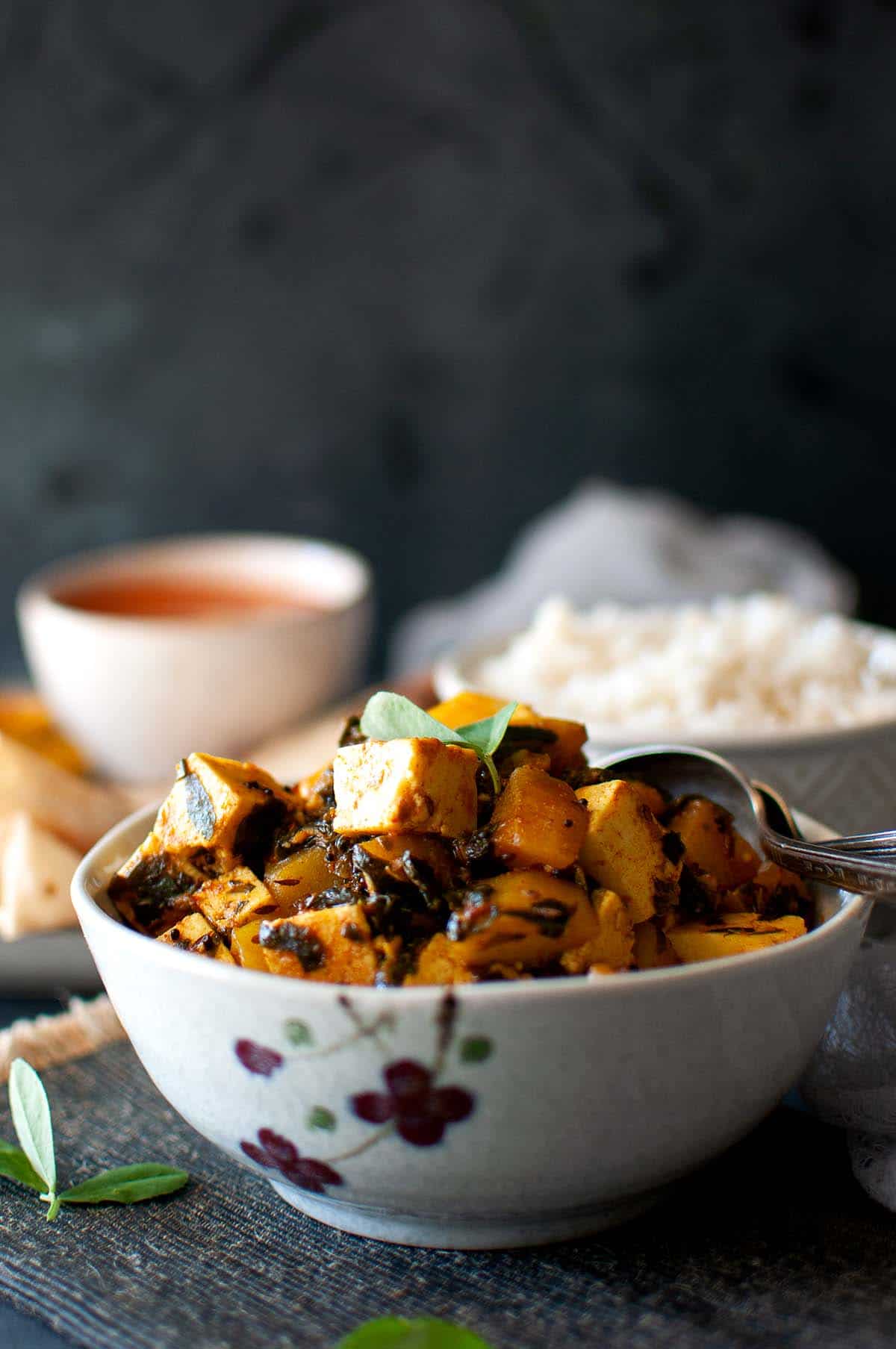 Grey bowl with potato methi paneer curry.