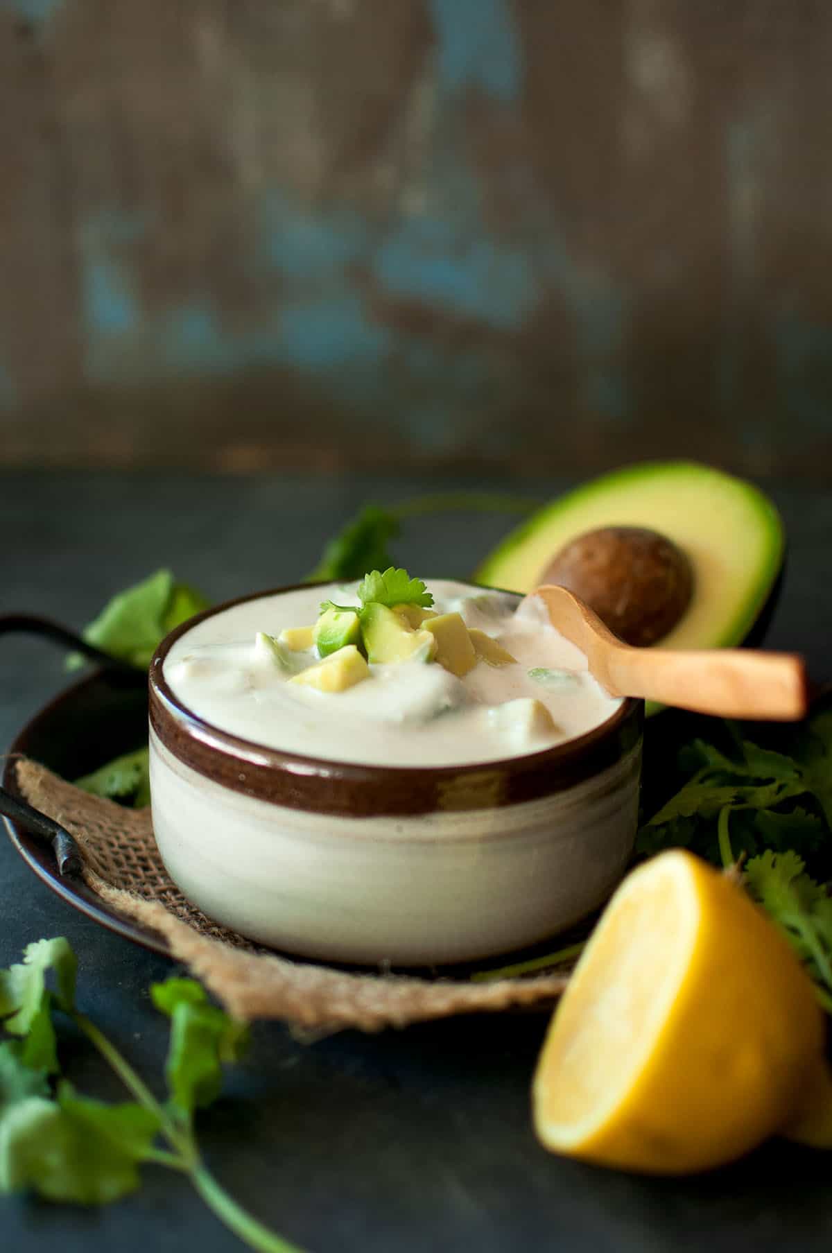 Brown bowl with raita sauce topped with chopped avocado.