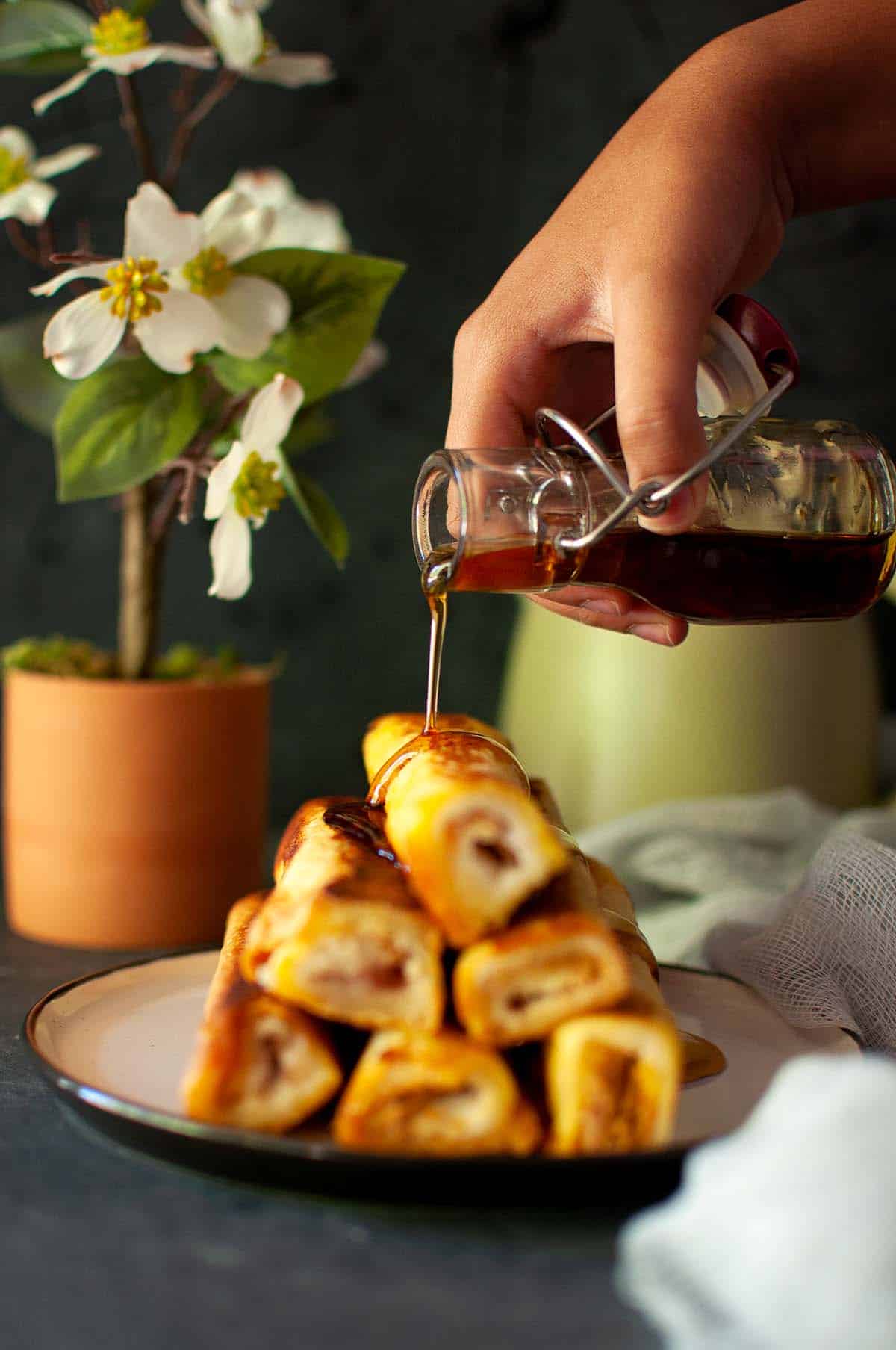 Hand pouring maple syrup on a stack of roll ups