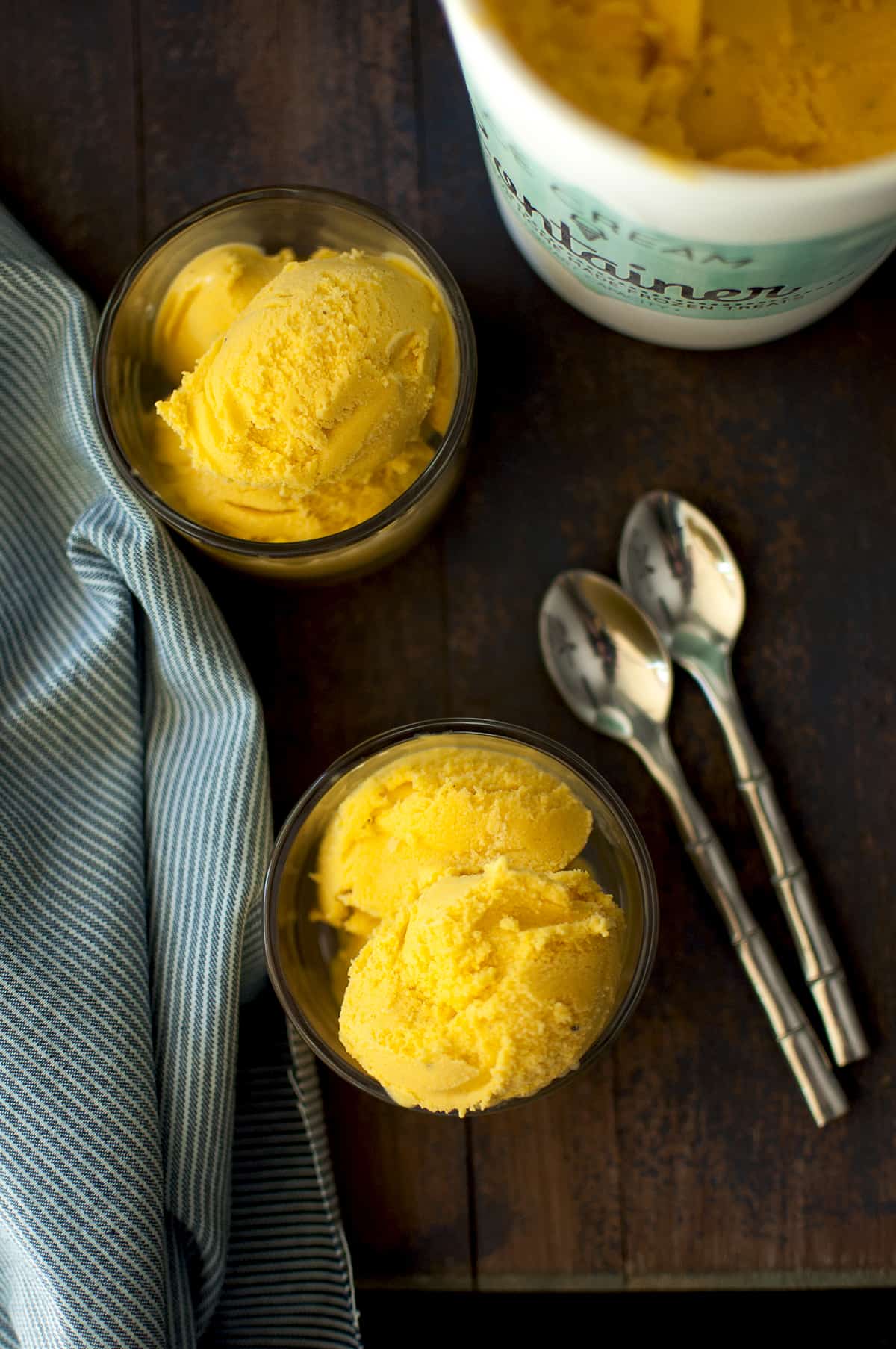 2 Glass serving bowls with scoops of mango gelato with a ice cream container in the background