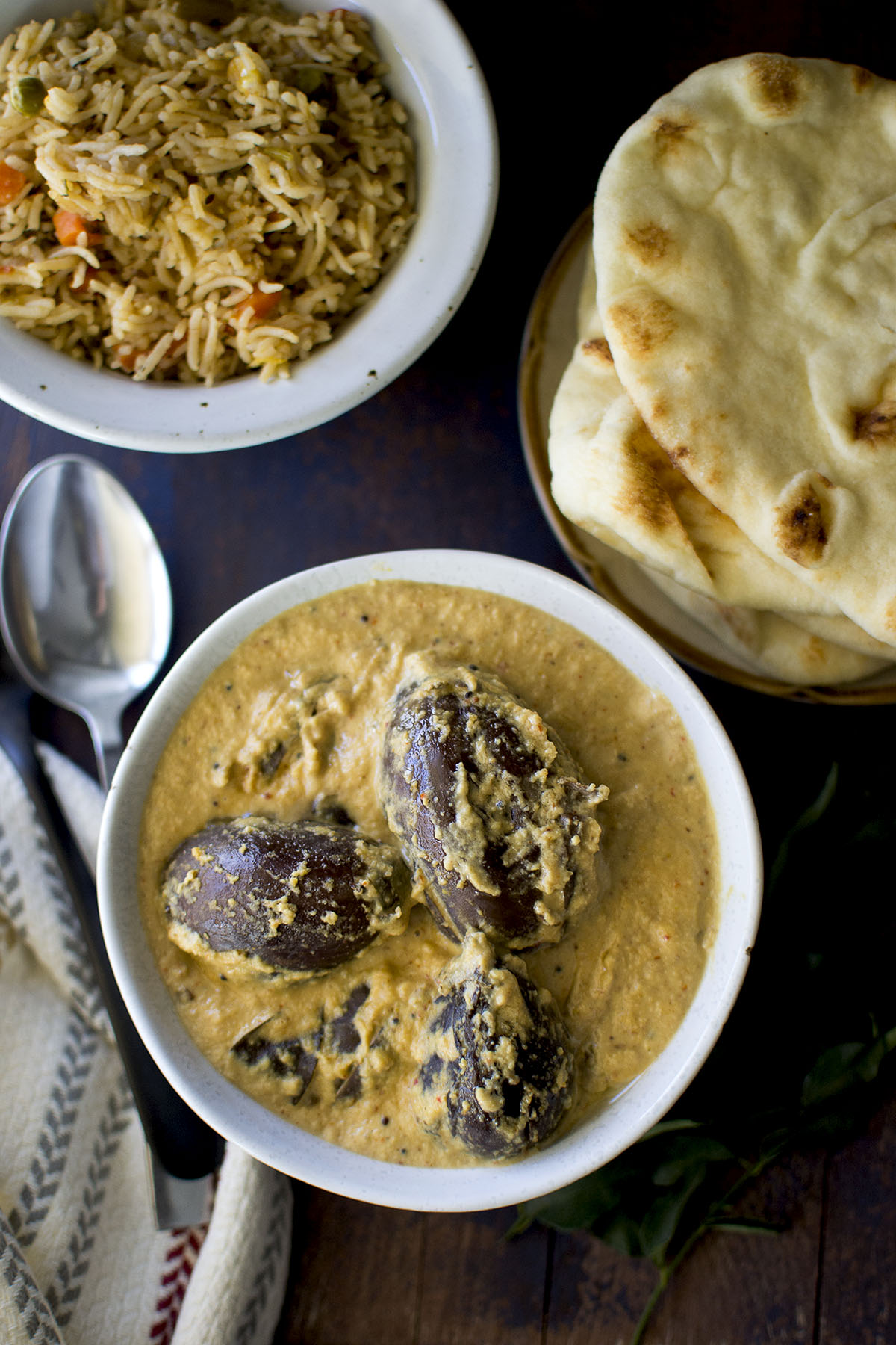 Top view of grey bowl with bagara baingan with naan and pualo.