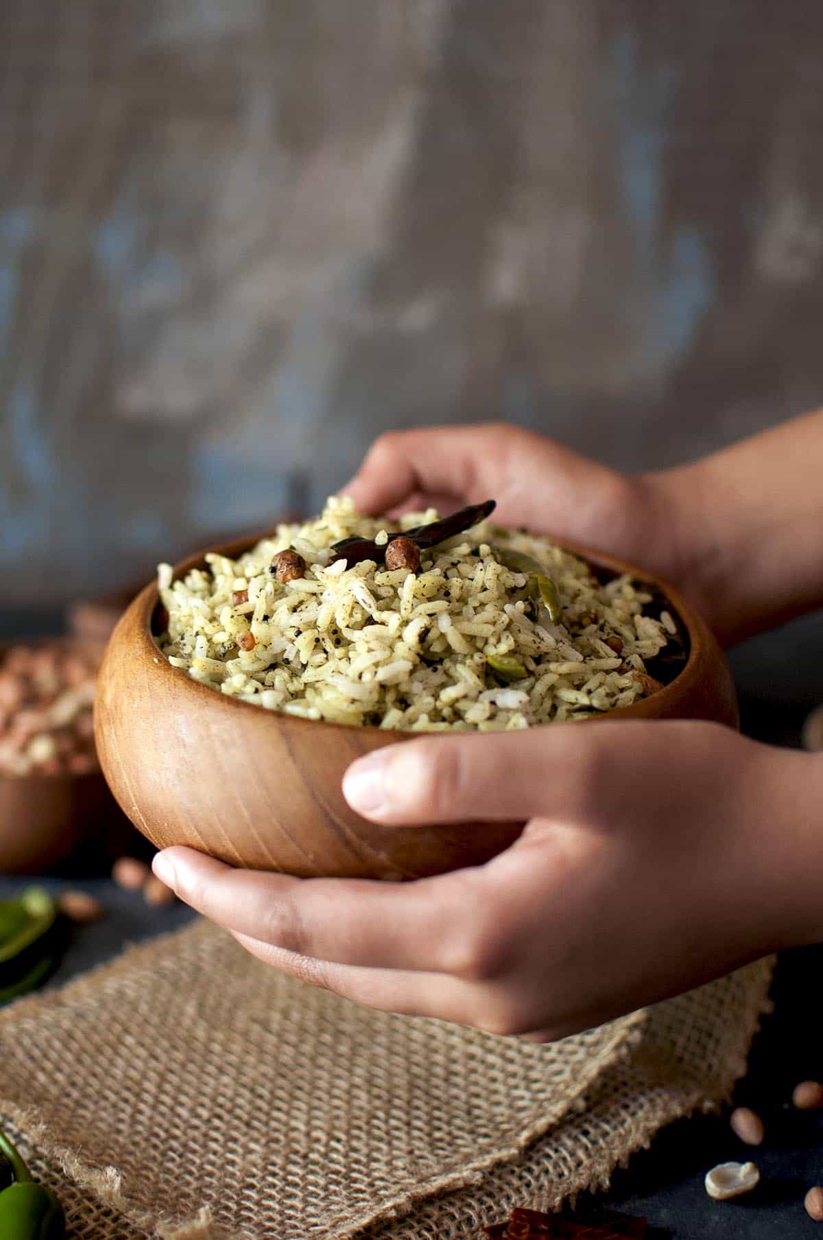 Hand holding a wooden bowl with gongura rice